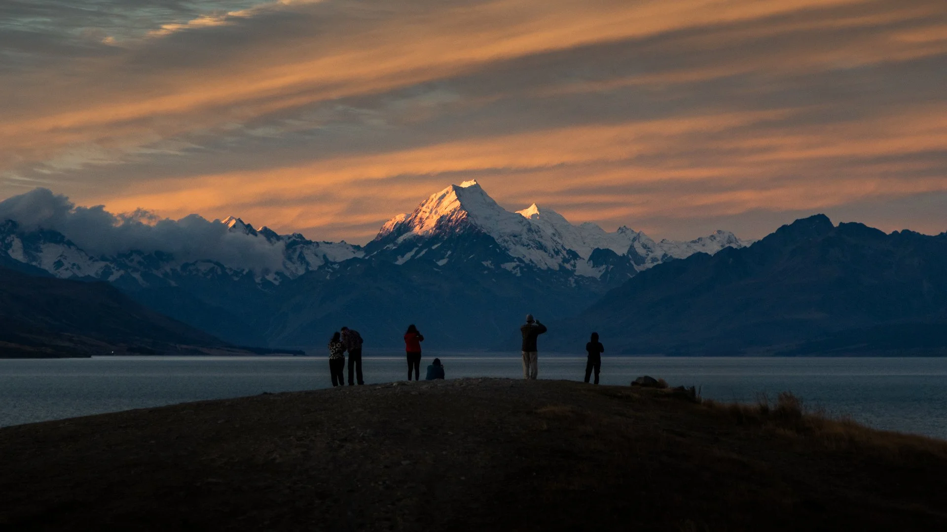 People watching the sunset at Lake Tekapo with snow-capped mountains in the background.