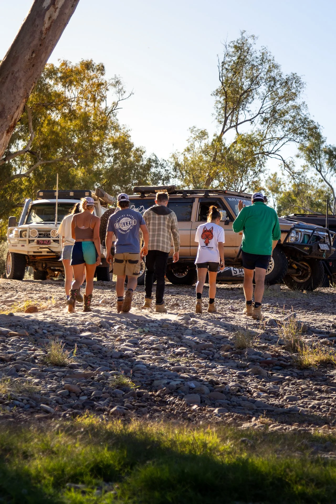Group of people walking towards off-road vehicles on rocky terrain in a natural outdoor setting with trees and blue sky.