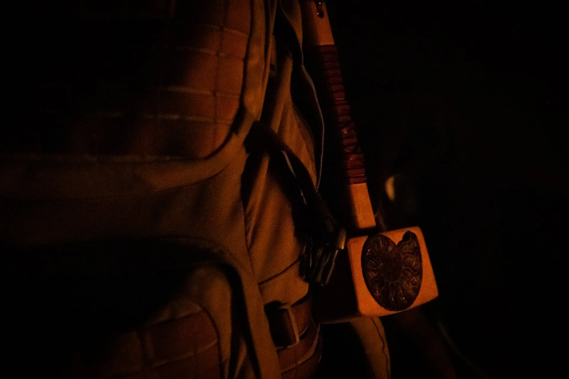 A dimly lit scene with a backpack, a book with a mandala or intricate design on the cover, and a small yellowish lamp or candle on a table.