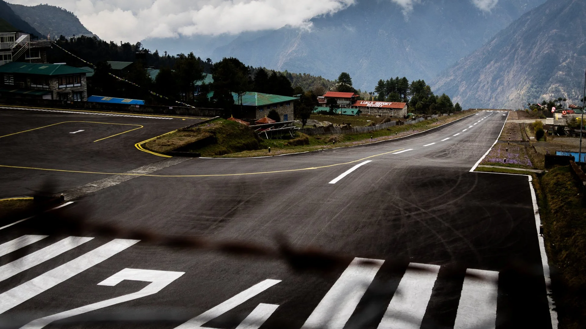Mountain road with buildings, trees, and cloudy sky.