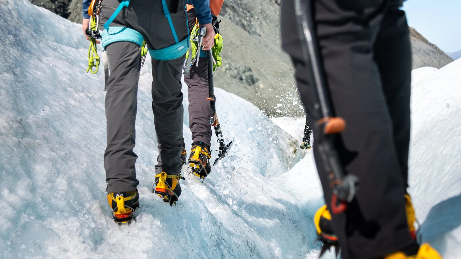 People in climbing gear and snowshoes hiking on icy snow or glacier in a mountainous area.