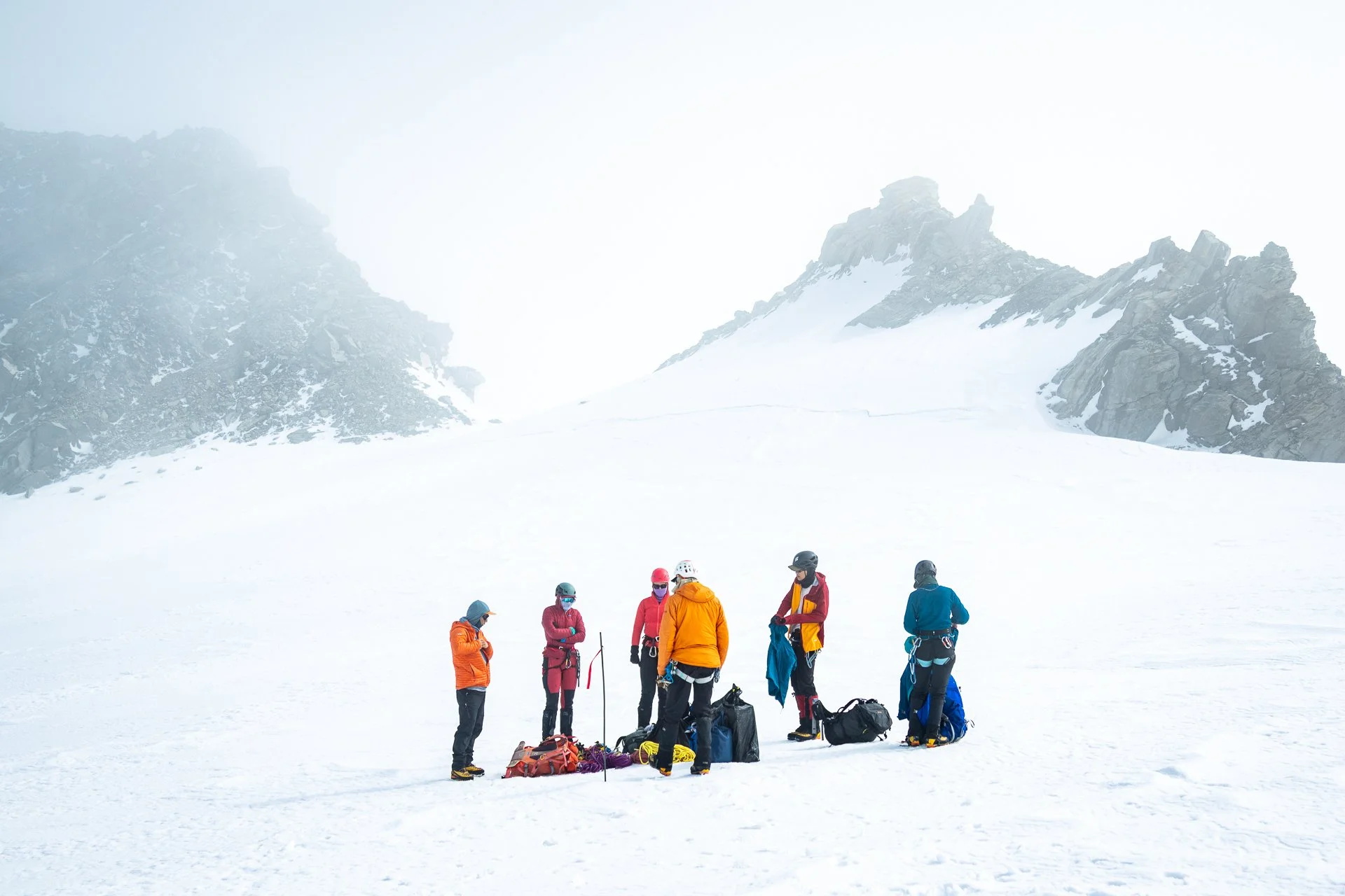 Group of hikers in winter gear standing on snow-covered mountain with rocky peaks in background.