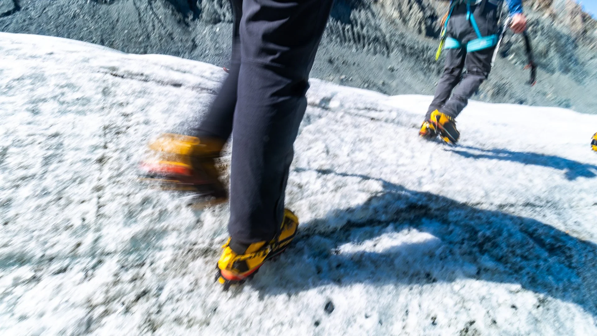 Close-up of two people mountain climbing on a snow-covered slope, wearing climbing gear and boots.