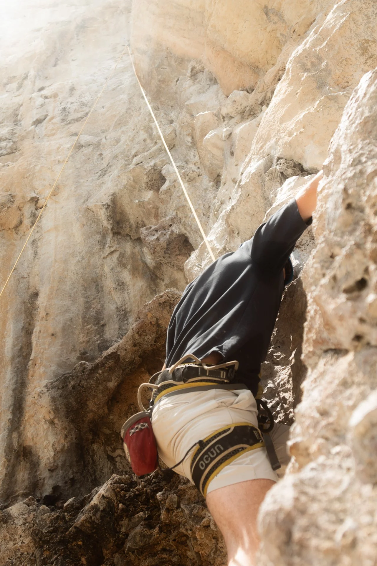 Person climbing a rocky indoor wall, wearing climbing gear and harness, with a safety rope.