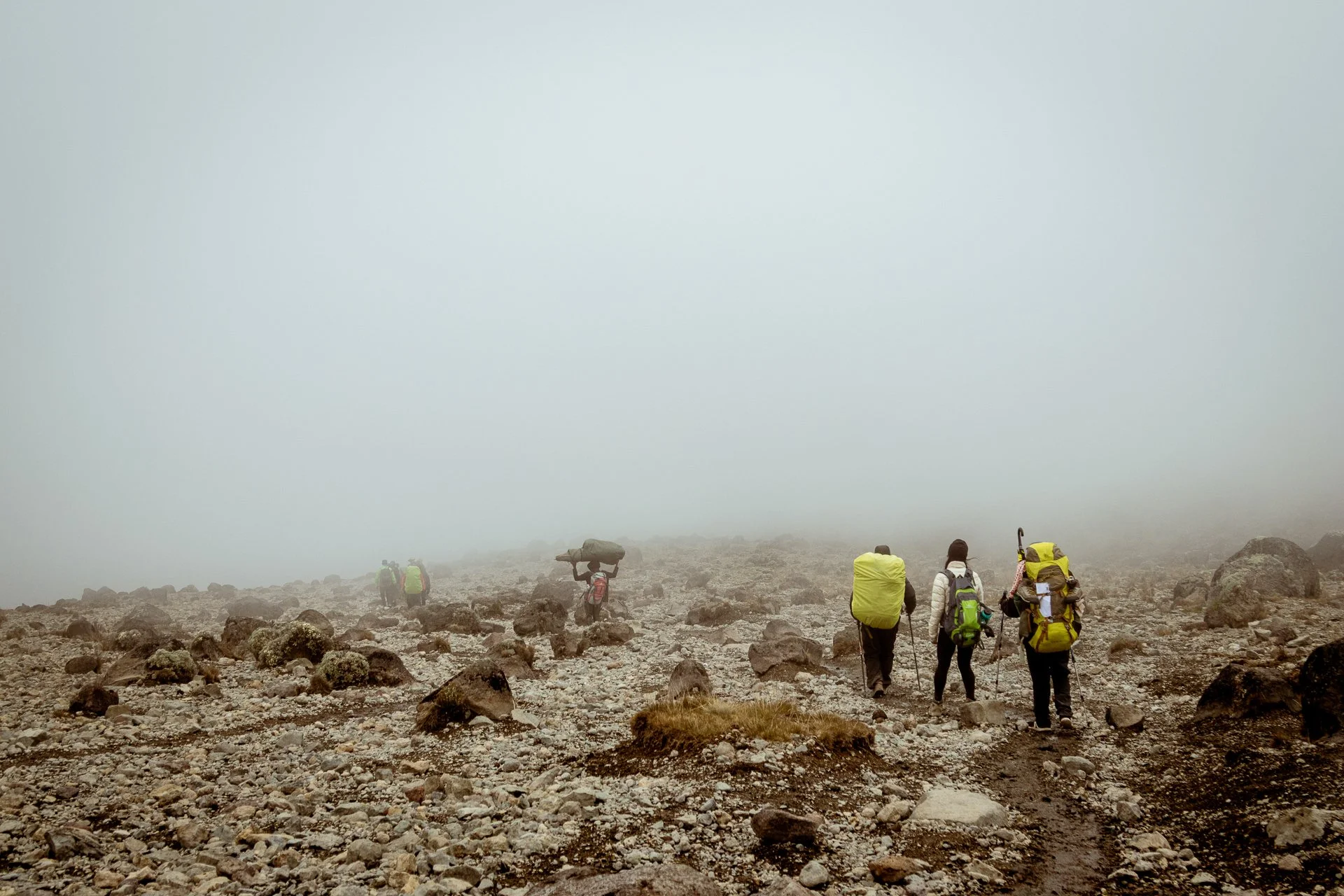 A group of hikers with backpacks walking on a rocky, cloudy mountain terrain.