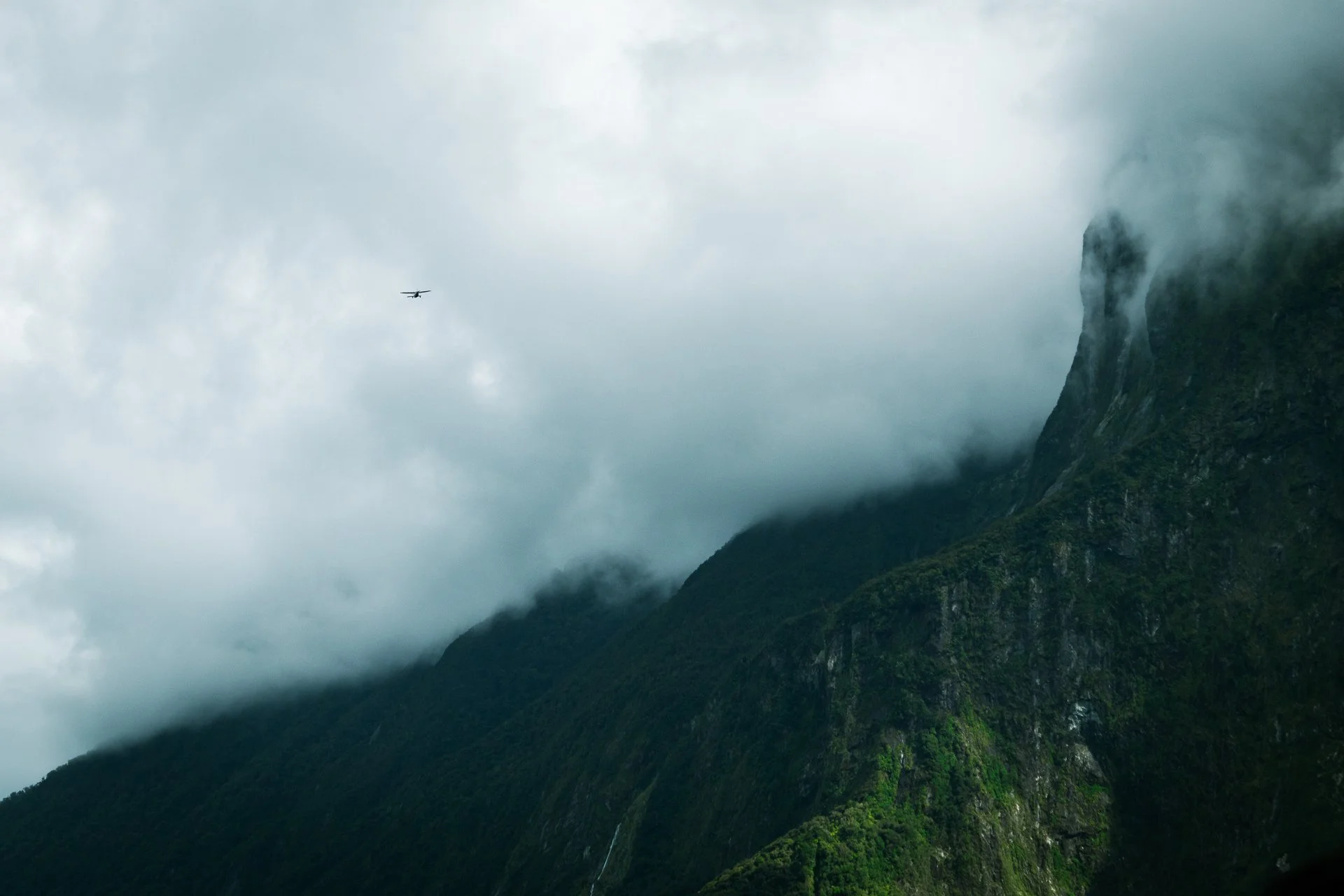 Cloudy sky over green mountain with a waterfall and a small airplane flying nearby