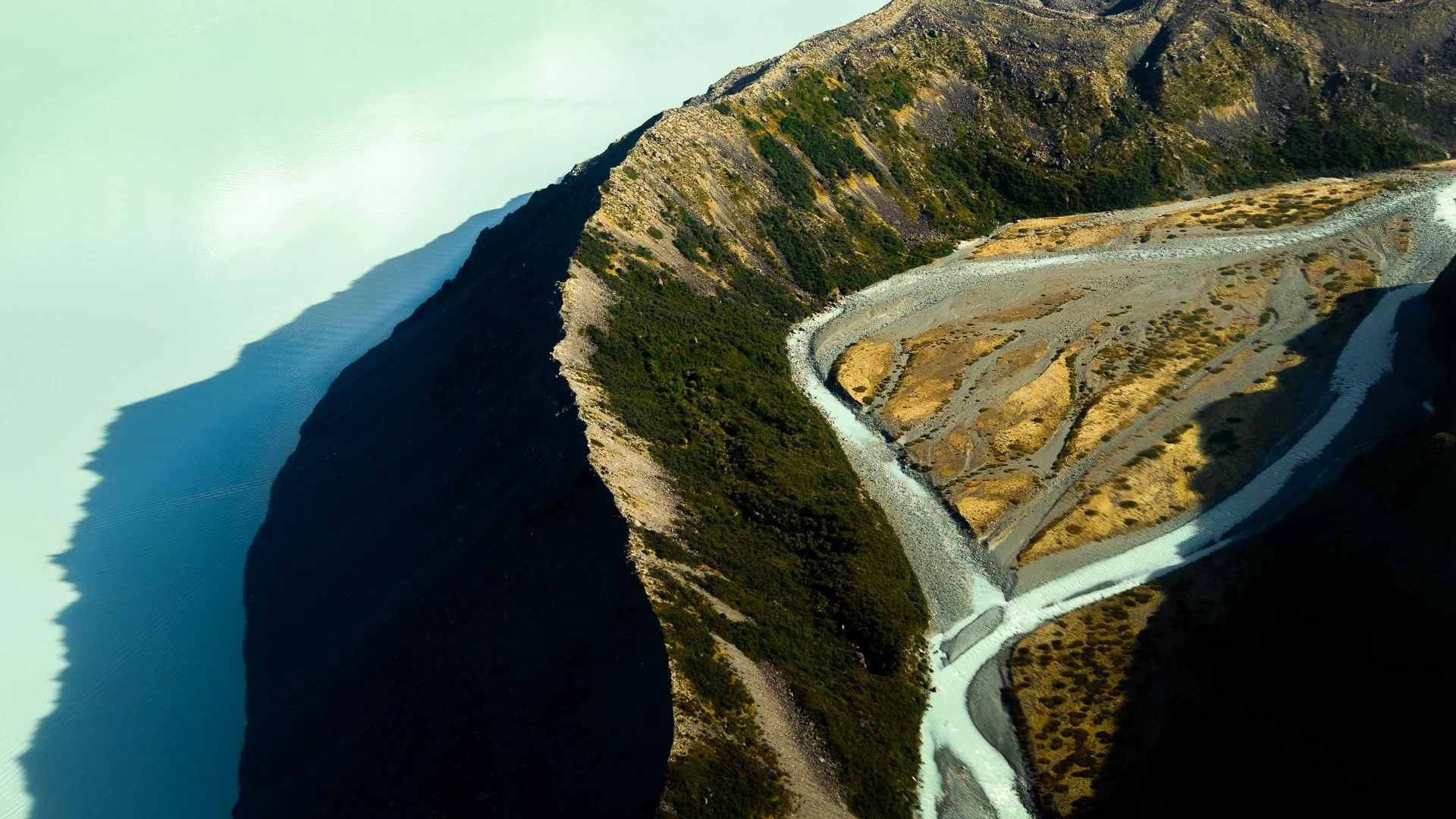 Aerial view of a dam creating a lake with steep mountain slopes surrounding it.