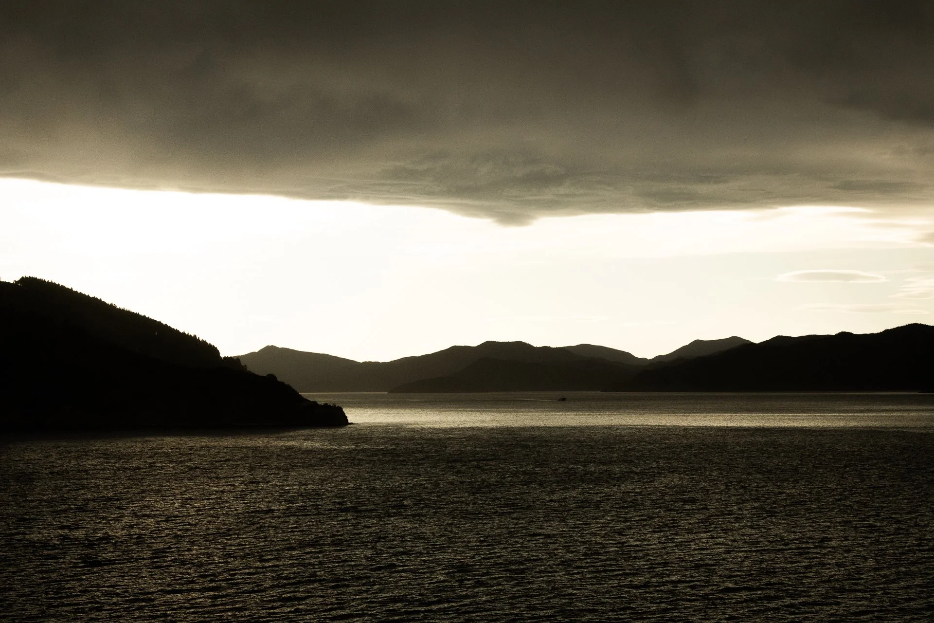 Dark storm clouds over a silhouette of a mountain range by a body of water during dusk or dawn.