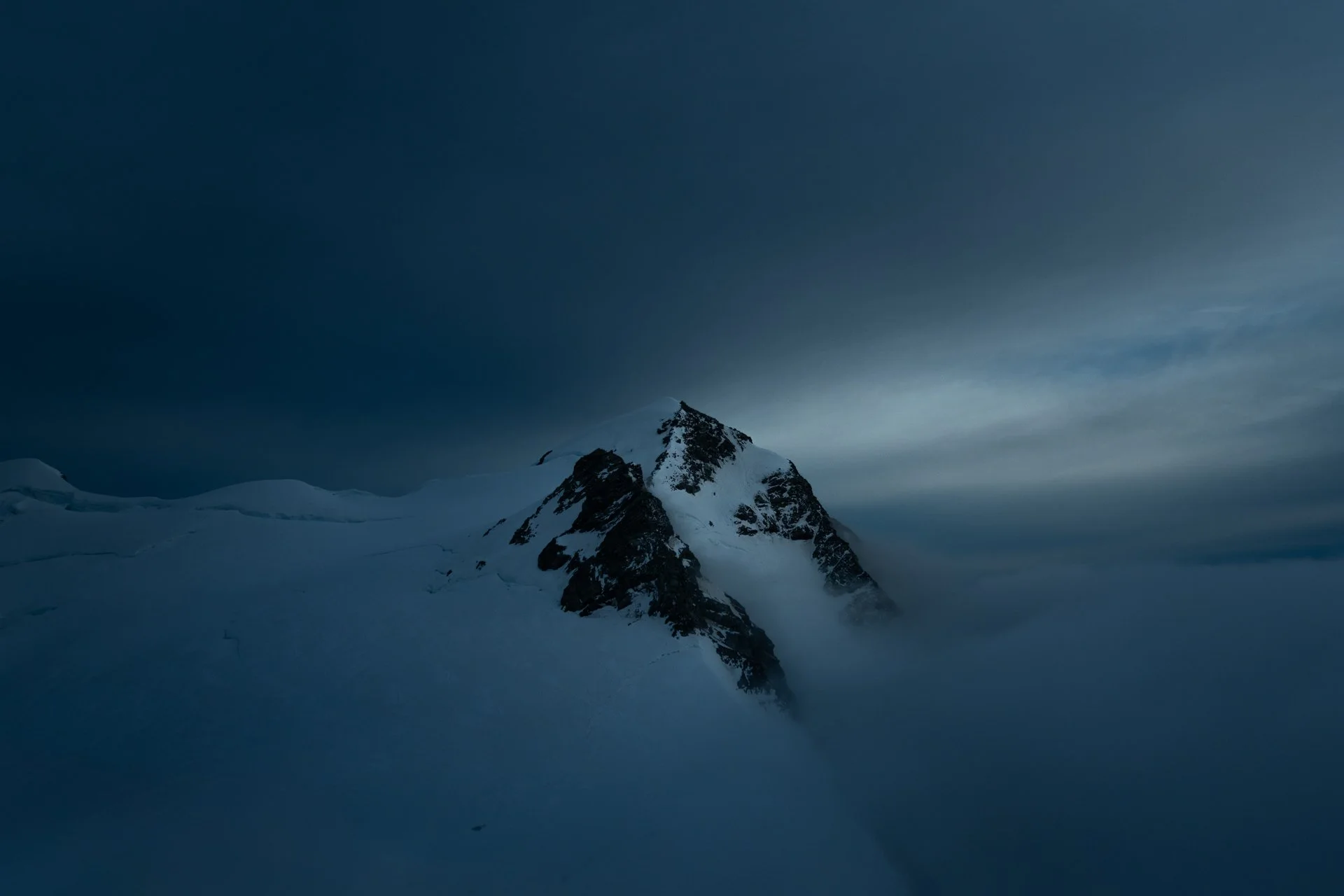 Snow-covered mountain peak under a dark, cloudy sky with fog.