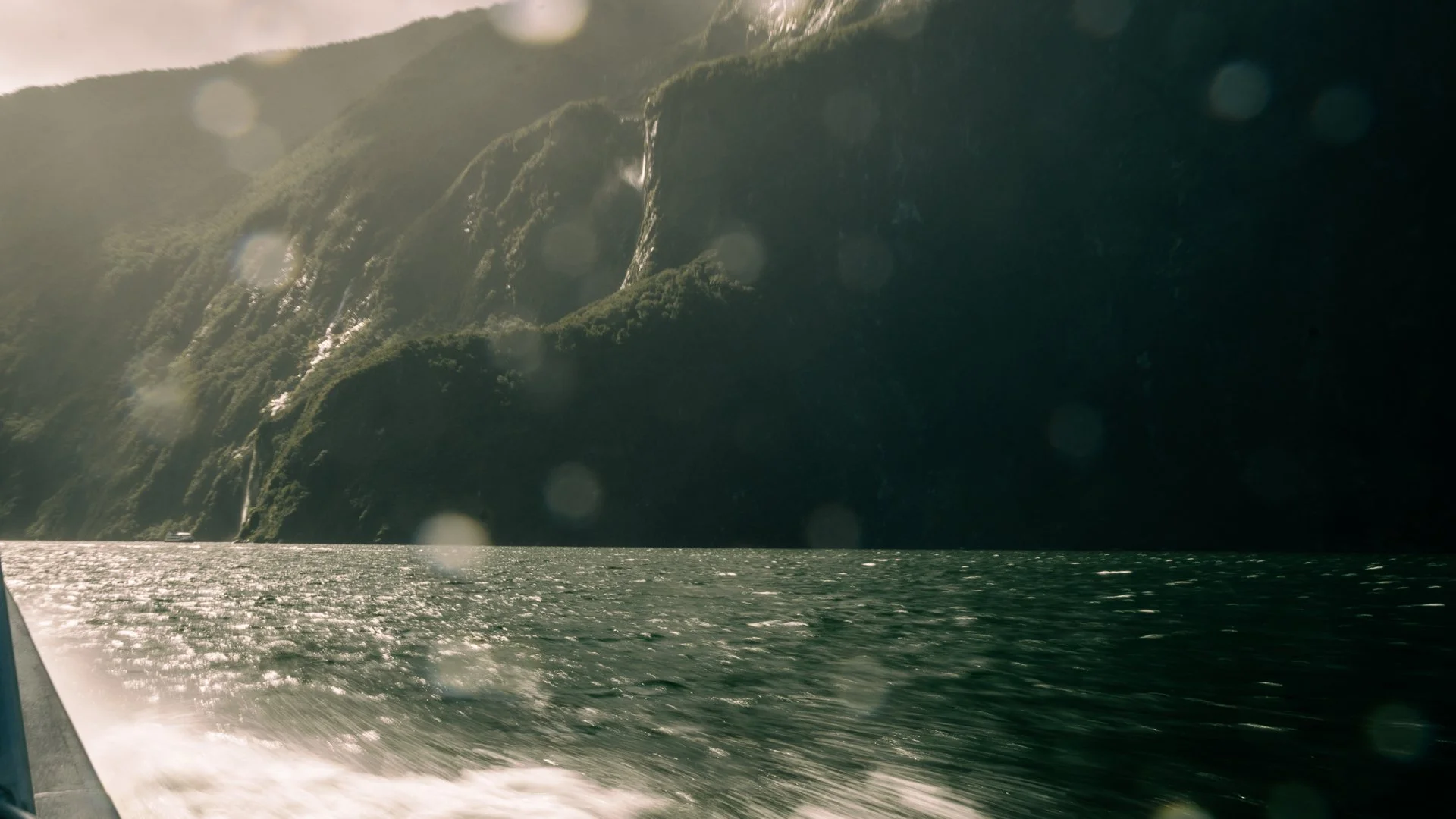 A scenic view of a mountain with cascading waterfalls viewed from a boat on a body of water.