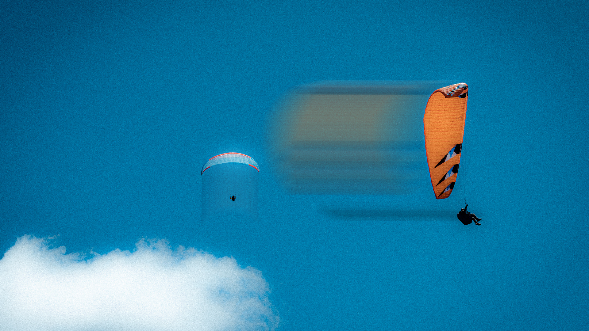 Two paragliders flying in a clear blue sky, with one flying higher and the other descending.