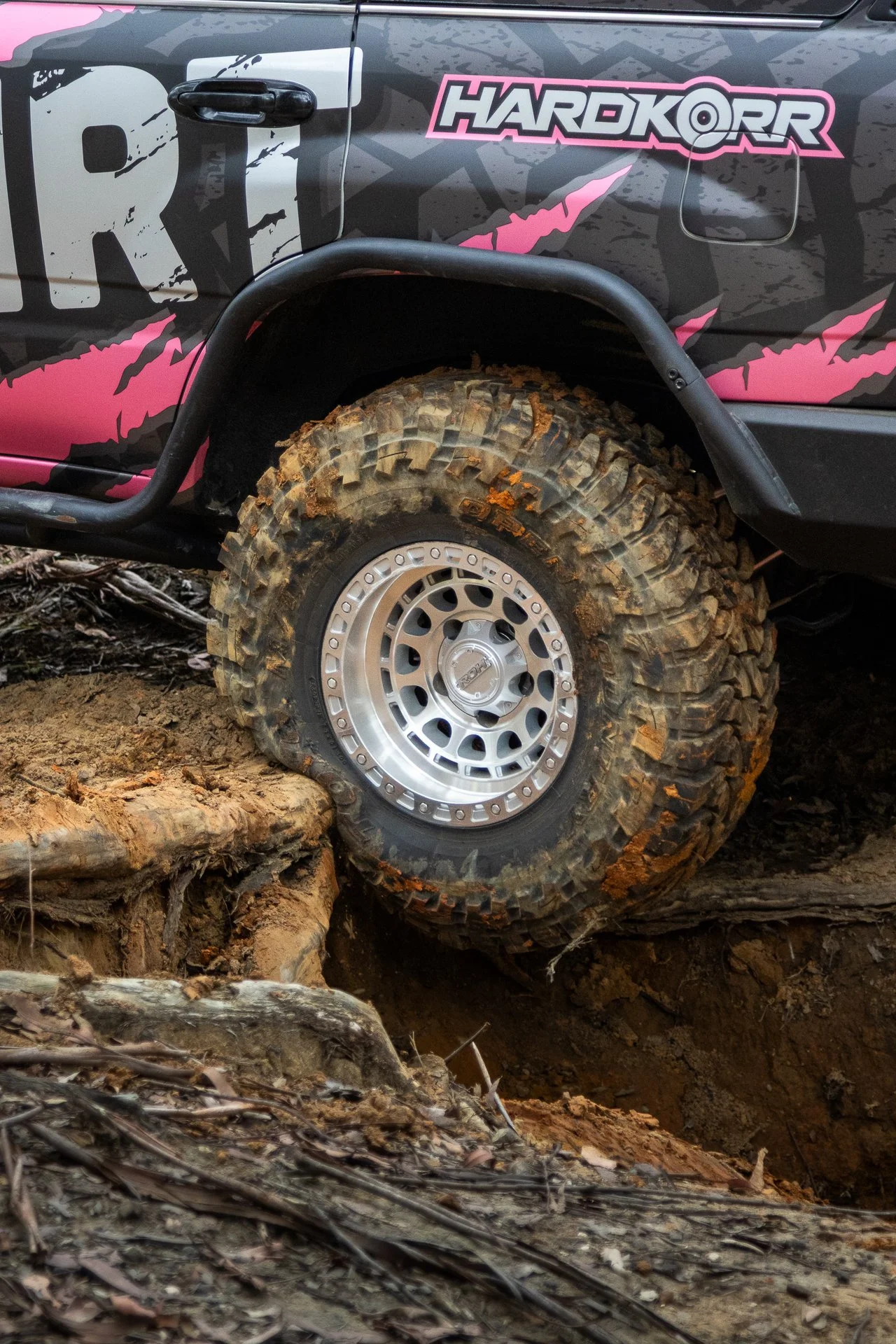 A vehicle with rugged tires navigating uneven, muddy terrain with rocks and dirt.