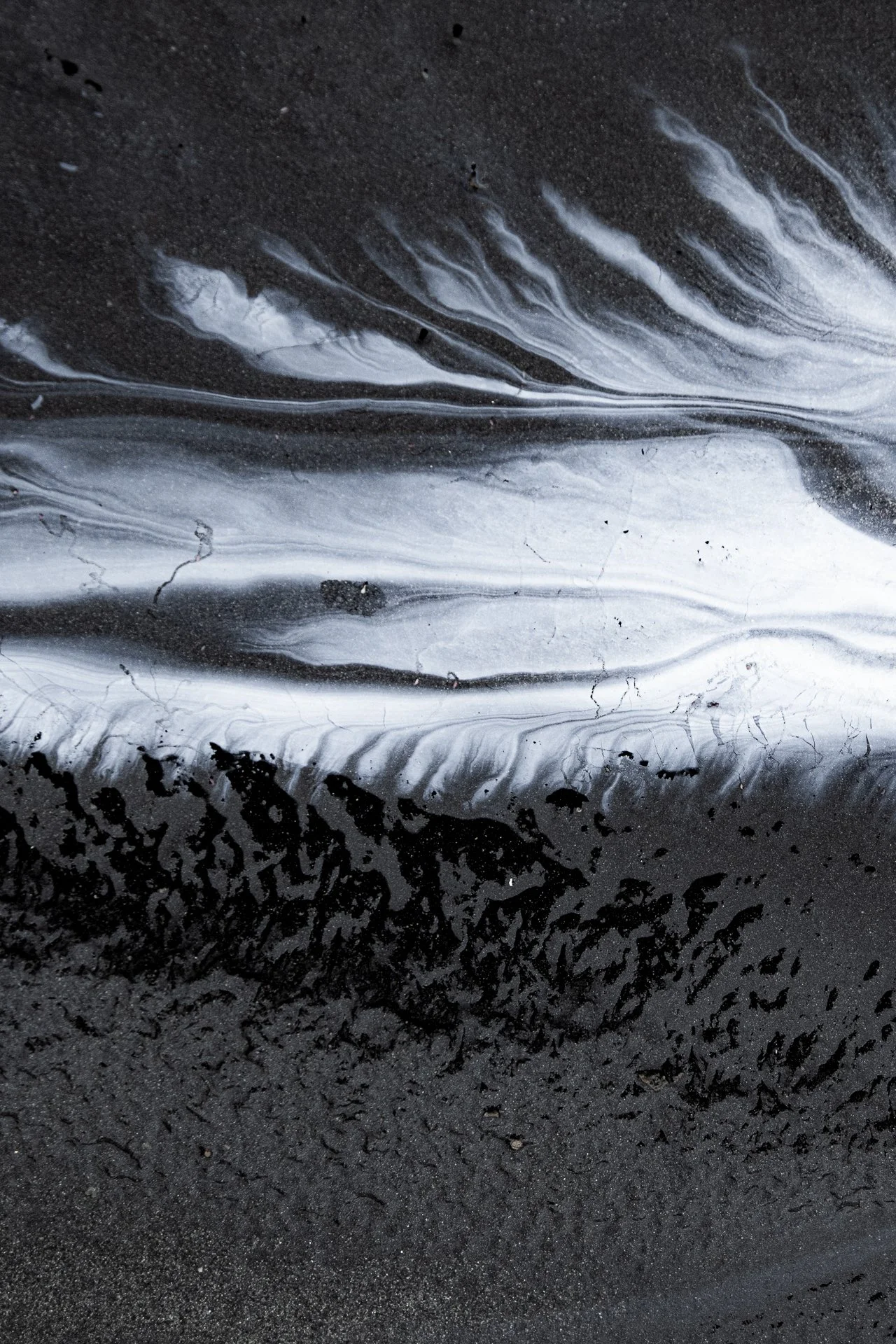 Close-up of wet black asphalt with streaks of white and gray paint or chalk, creating abstract patterns.