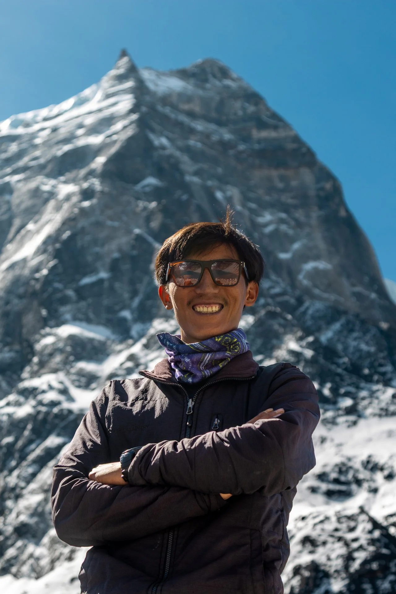 Smiling woman wearing sunglasses and a jacket outdoors in snowy mountain landscape.