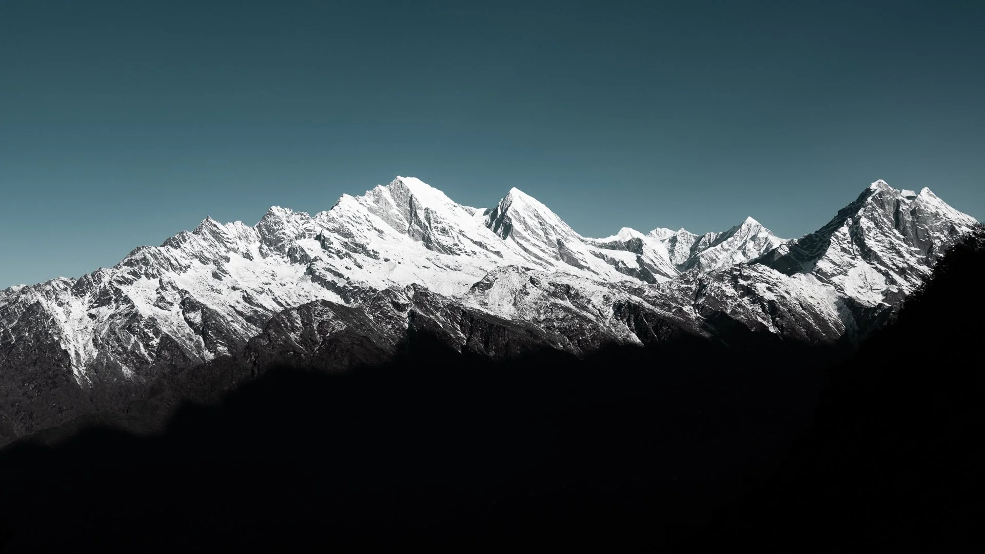 Snow-capped mountain range under a clear sky, with dark foreground hills.