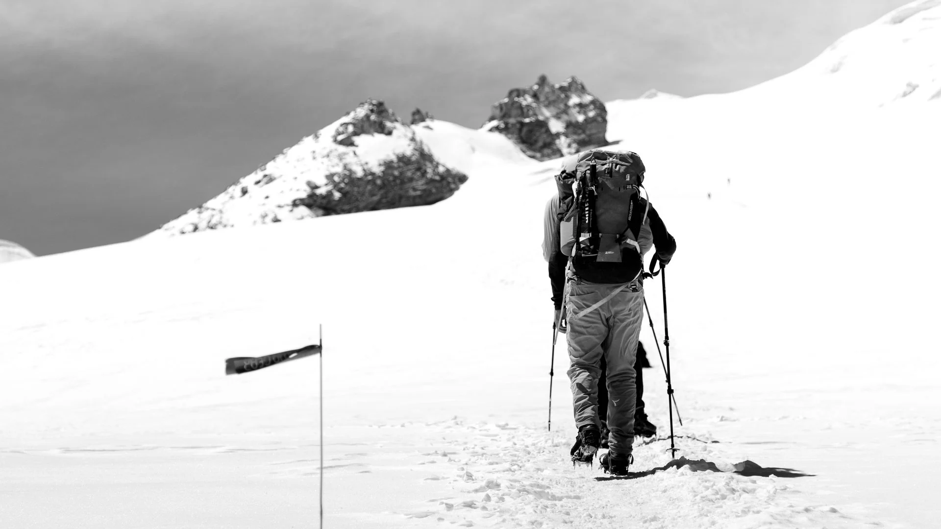 A group of people in winter gear hiking on a snow-covered landscape with mountain peaks in the background.