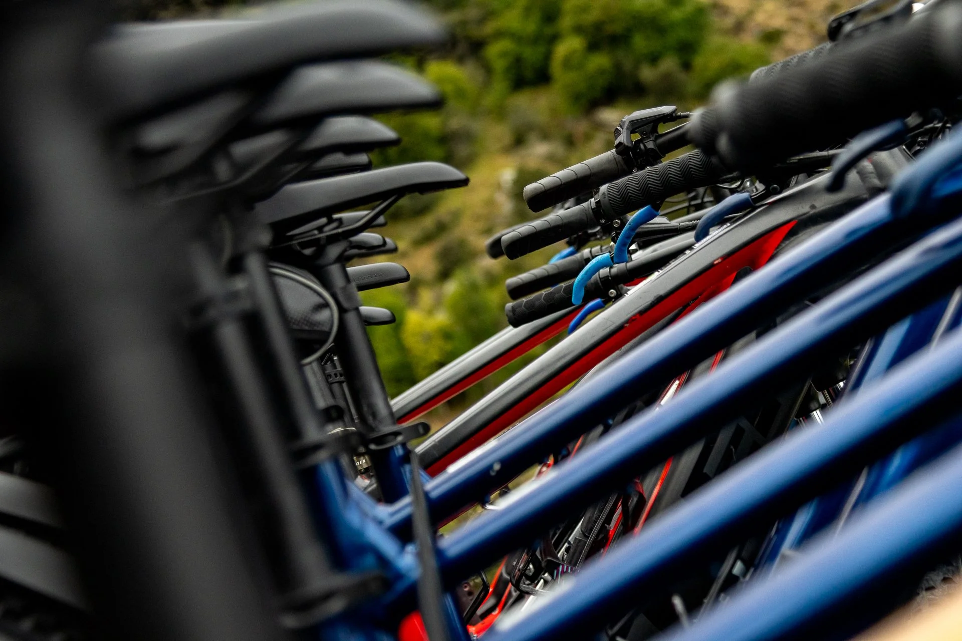 Row of bicycles parked outdoors, focusing on the bicycle handlebars, saddle, and frames with a blurred green natural background.