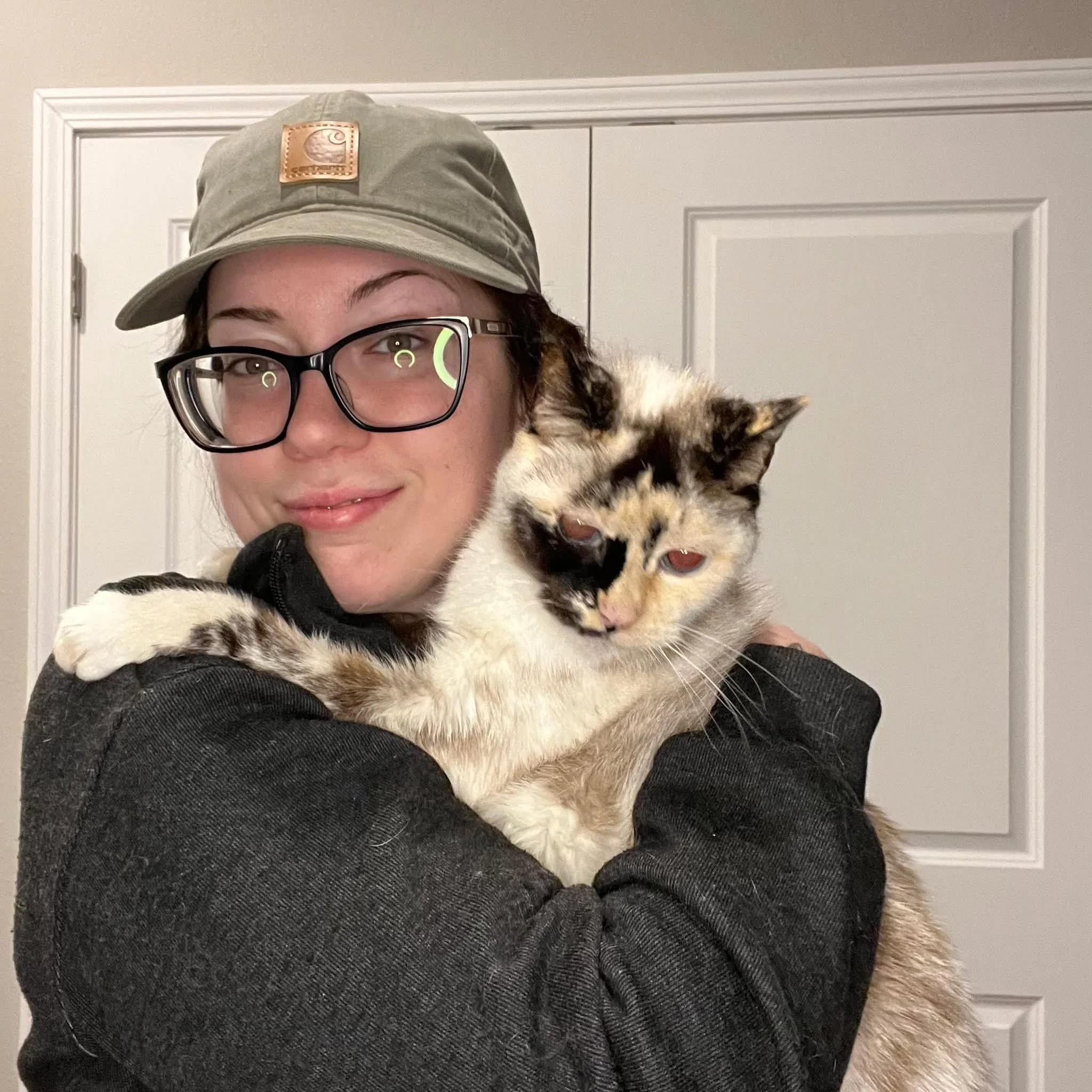 Woman with hat and black-rimmed glasses holding cat
