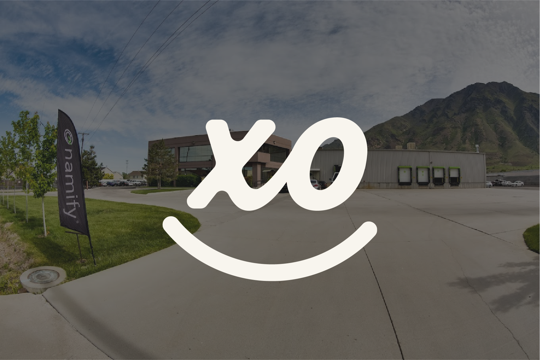 A building with a mountain in the background, a black flag with 'namify' written on it, and a parking lot with delivery docks.