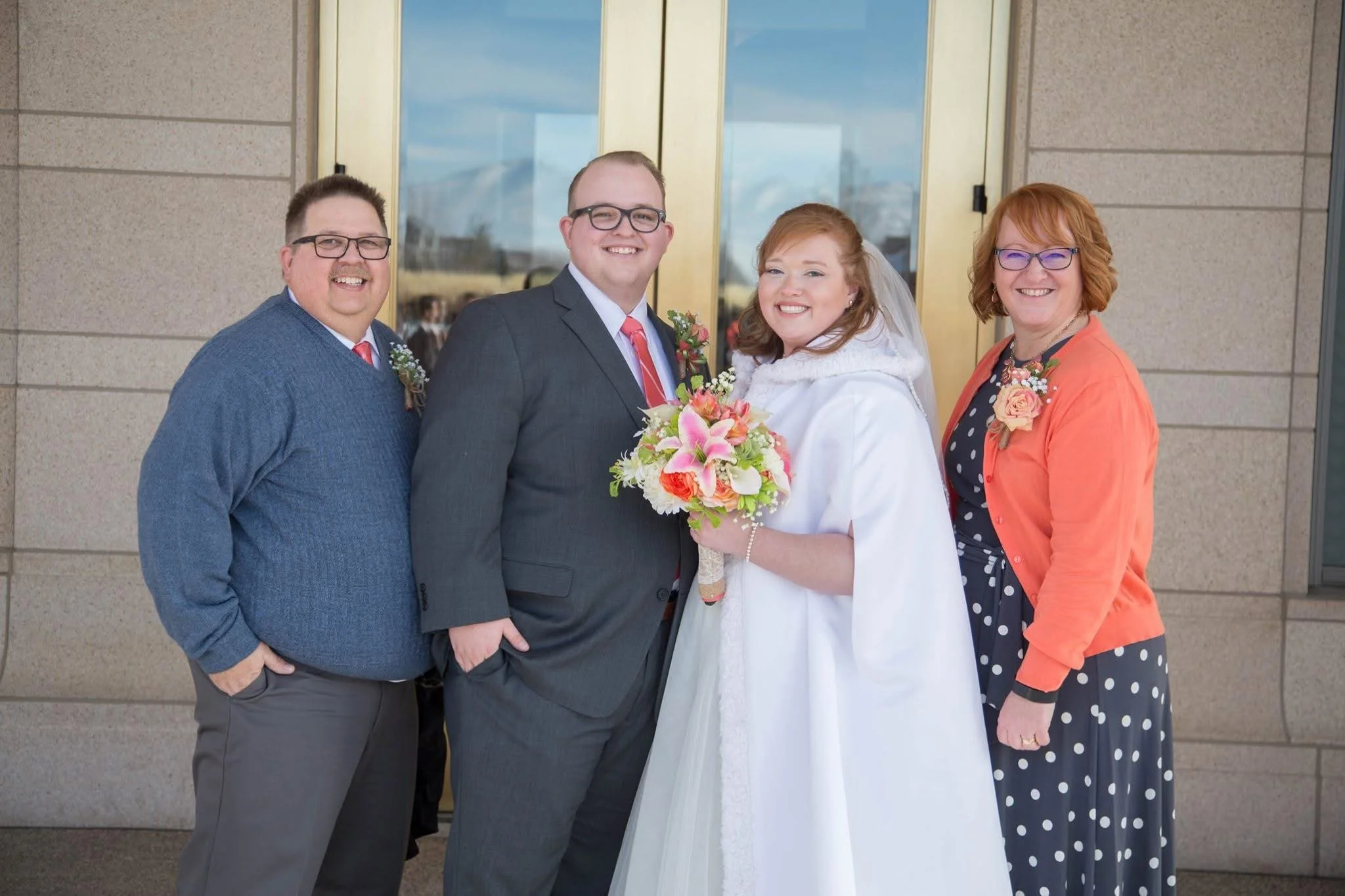 Giles, Kayla, and Giles' parents standing together in front of the Oquirrh Mountain Temple, Kayla is in a white wedding dress holding a bouquet.