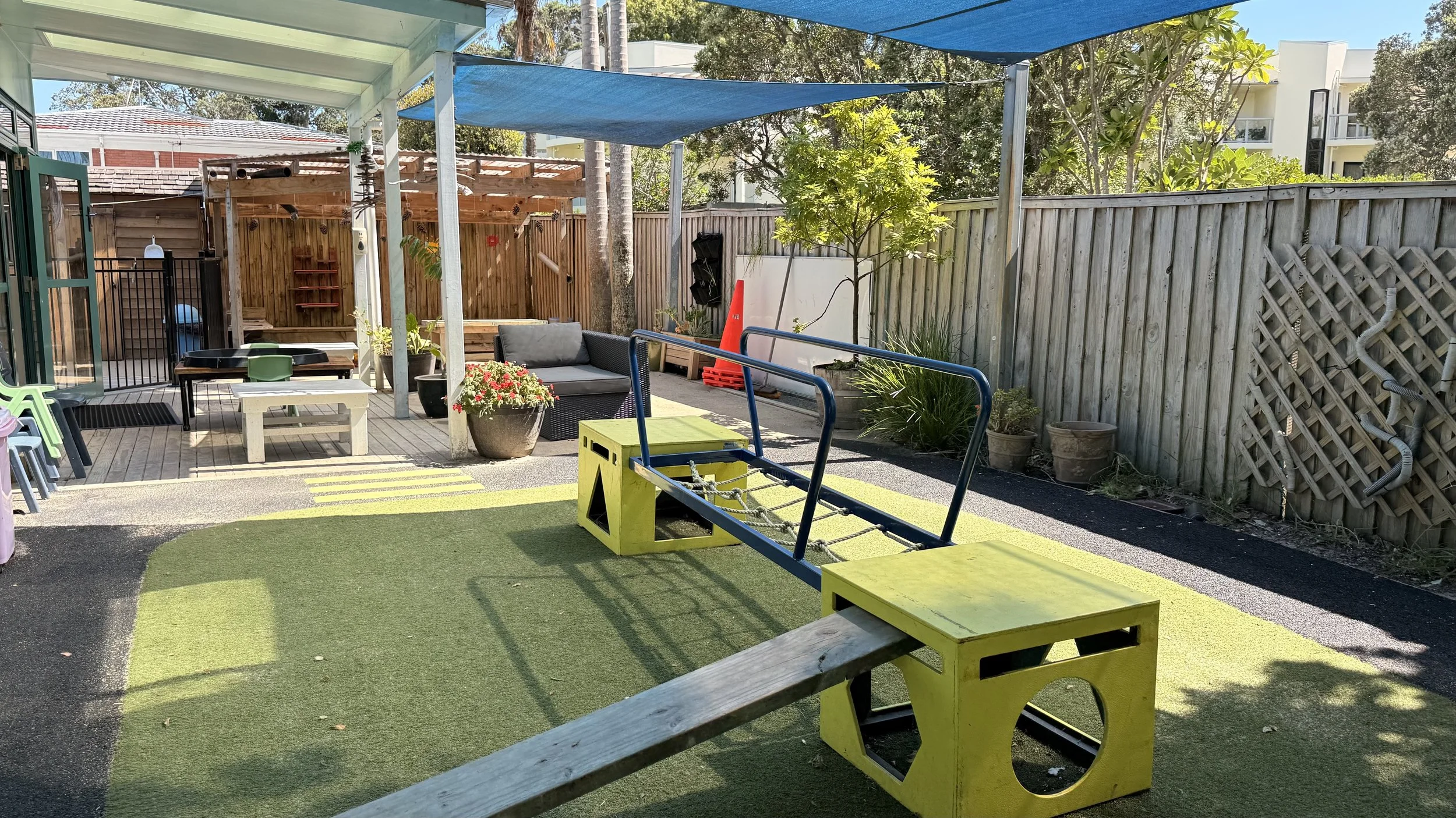 Children's playground area with bright yellow balance beam and platform at Kiwi Kids Early Learning in Takapuna at Kids Group.