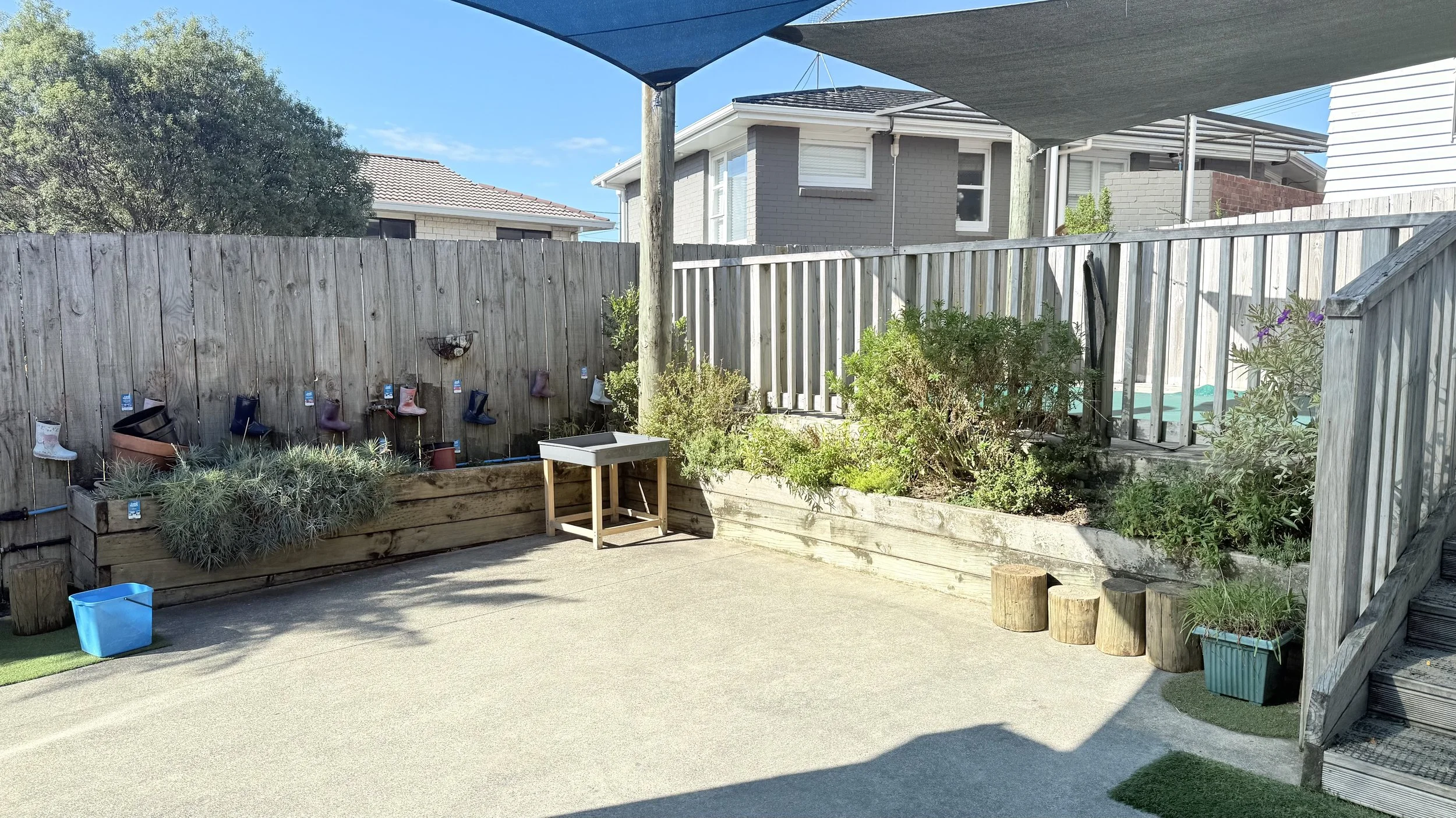 Backyard with wooden fence, planted garden beds, potted plants, a small water sink, and hanging rain boots as decoration.