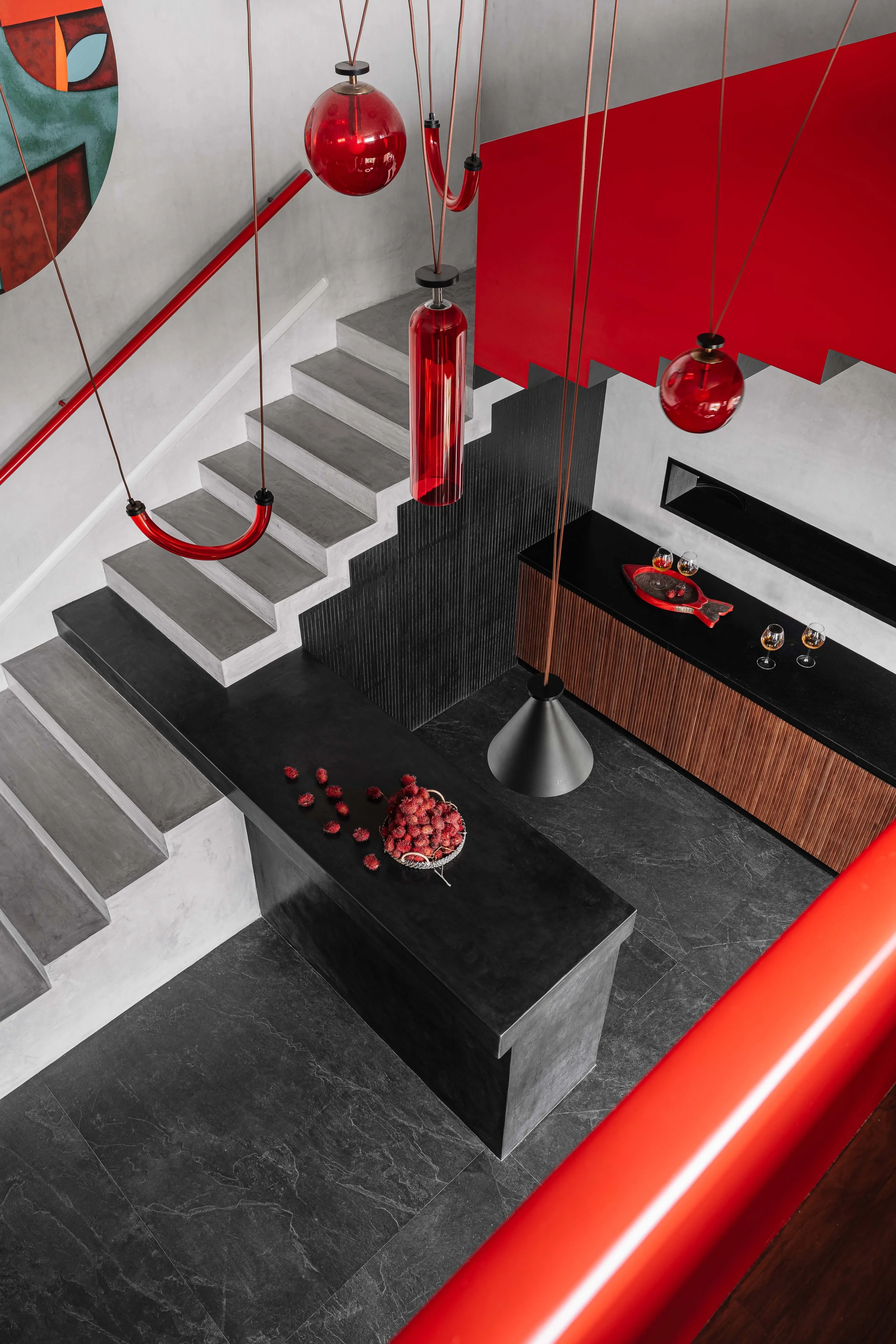 Elevated view of the sculptural staircase with red glass pendant lights, bold red accents, and dark stone finishes at Gardens in the Sky, a Calicut residence designed by Workers of Art.