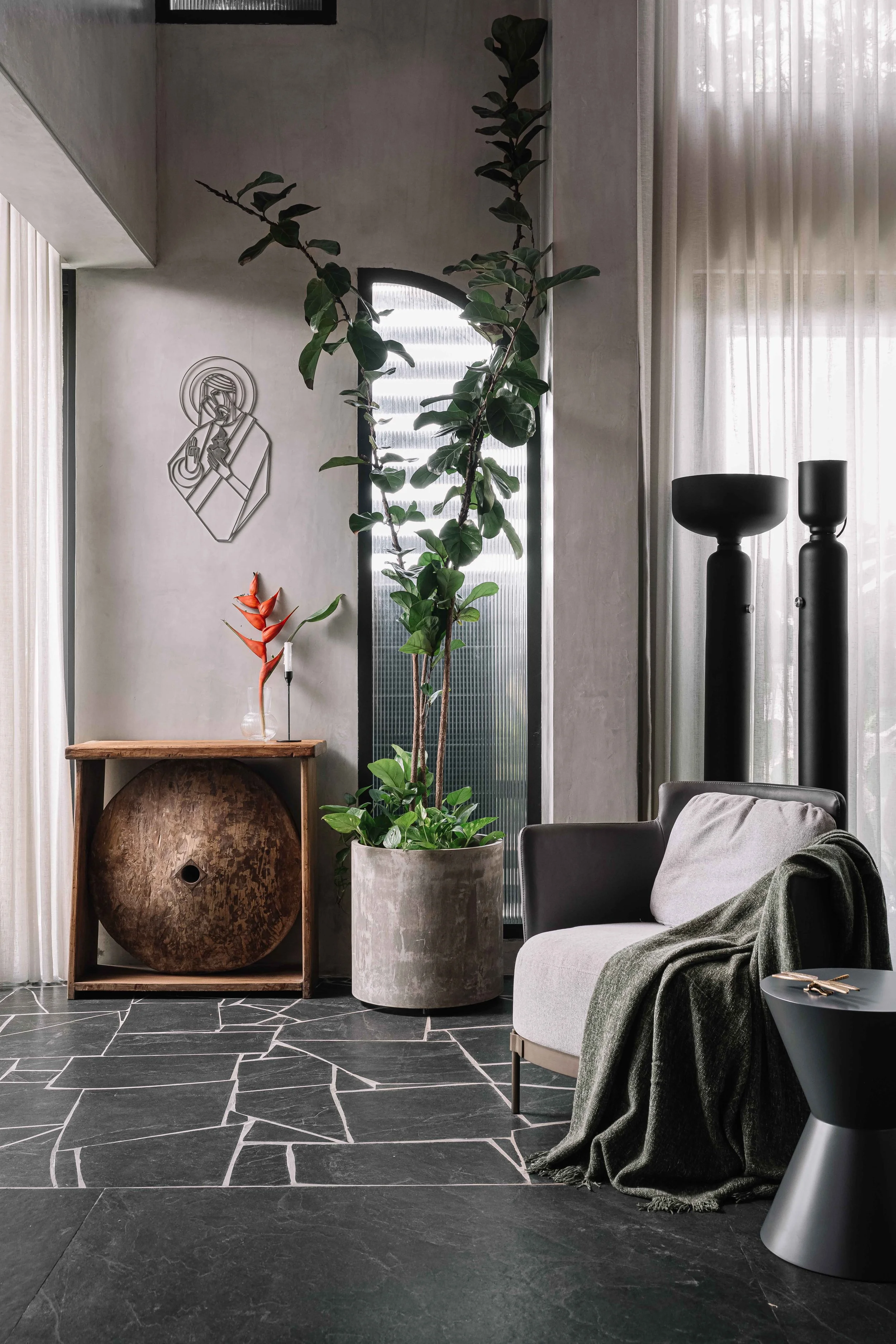 Living corner with a lounge chair, indoor plant, sculptural console and black stone flooring in Gardens in the Sky, a Calicut residence by Workers of Art.