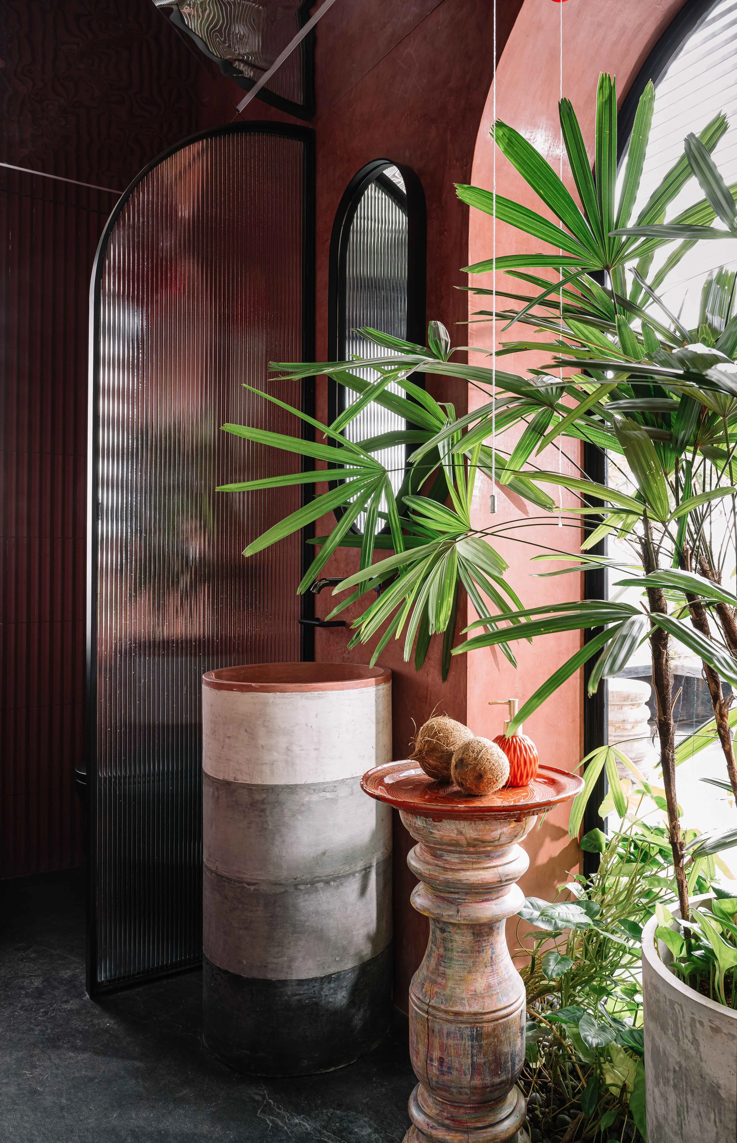 Interior garden corner with arched ribbed-glass doors, terracotta walls, tropical plants, and sculptural decor at Gardens in the Sky, a Calicut residence designed by Workers of Art.