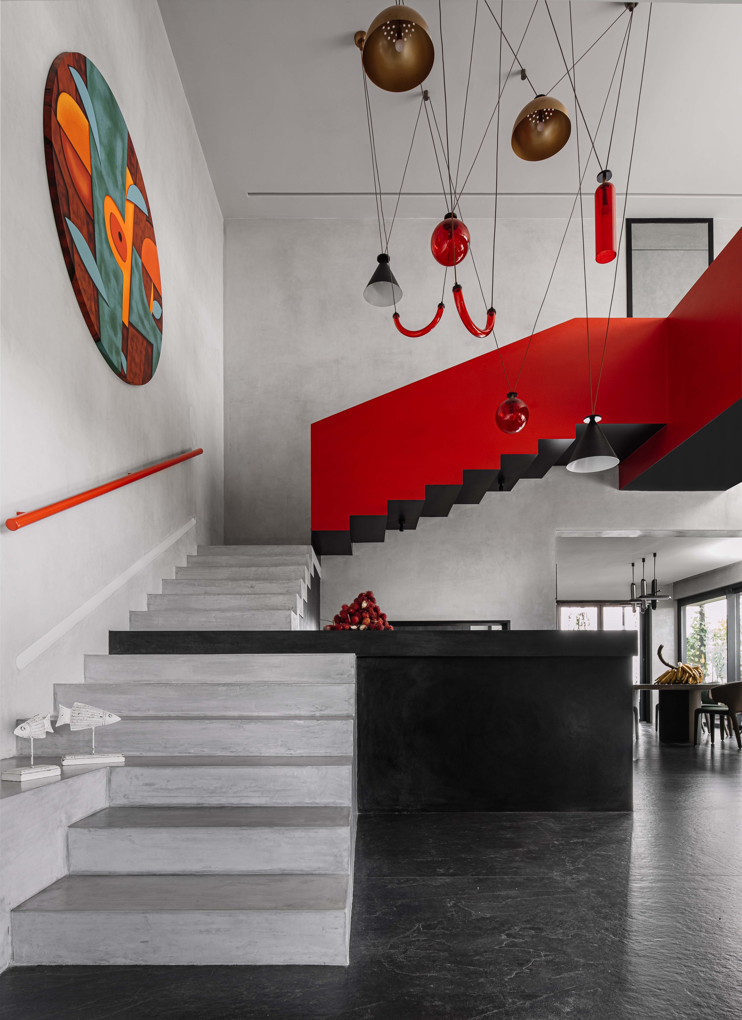 Staircase interior with a bold red railing, sculptural pendant lights, and artwork at Gardens in the Sky, a Calicut residence designed by Workers of Art.