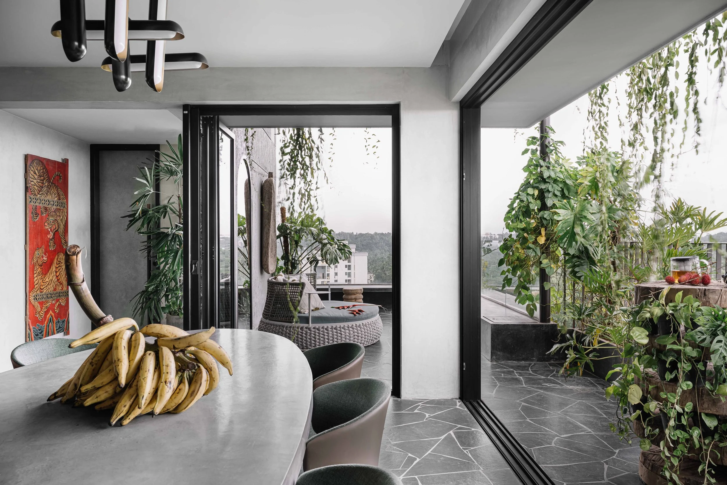 Contemporary dining area opening onto a lush terrace, with sculptural lighting and expansive glazing at Gardens in the Sky, a Calicut residence designed by Workers of Art.