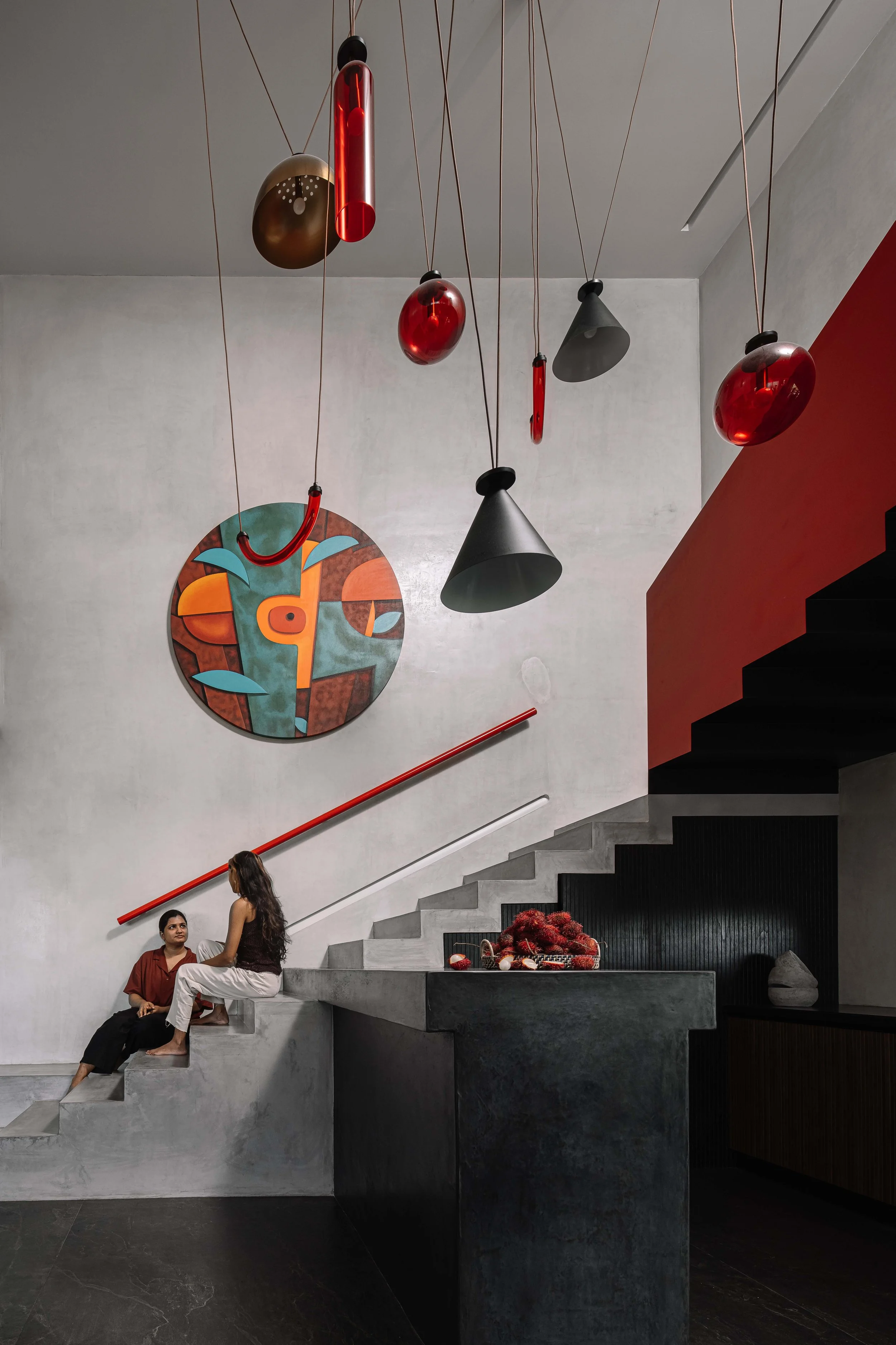 Sculptural staircase with bold red accents, statement pendant lights, and artwork at Gardens in the Sky, a Calicut residence designed by Workers of Art.