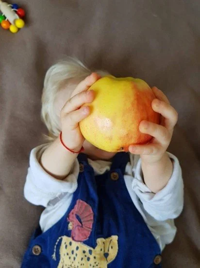 Child holding an apple in front of their face, partially covering it.