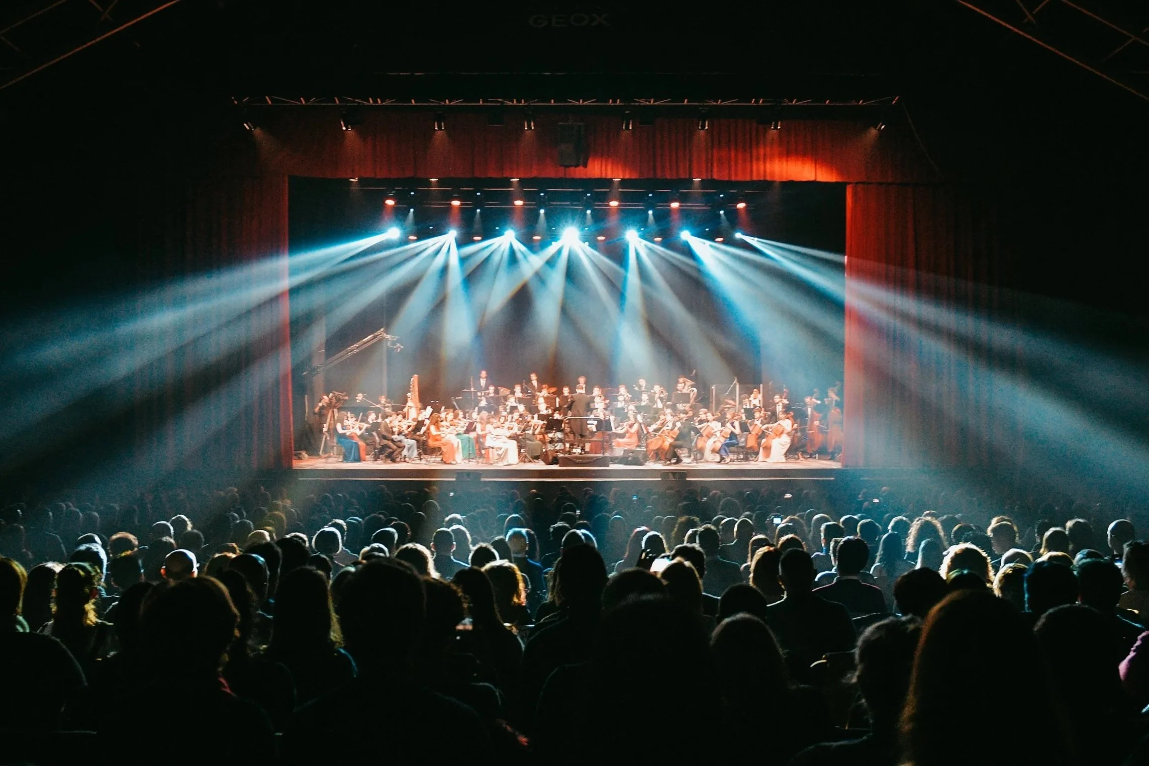 Fari di luce sul pubblico in piedi del Gran Teatro Geox con GSO ora URANICA al completo sul palco