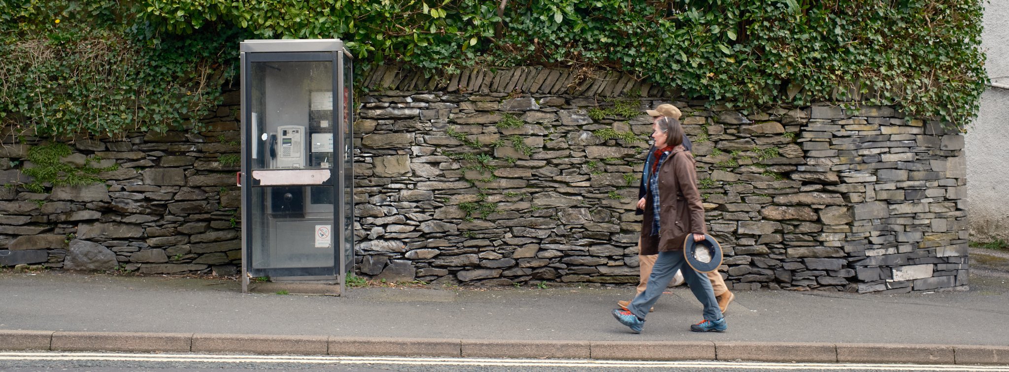 Couple walking past a stonee wall and phonebox in Windermere in the lakes district