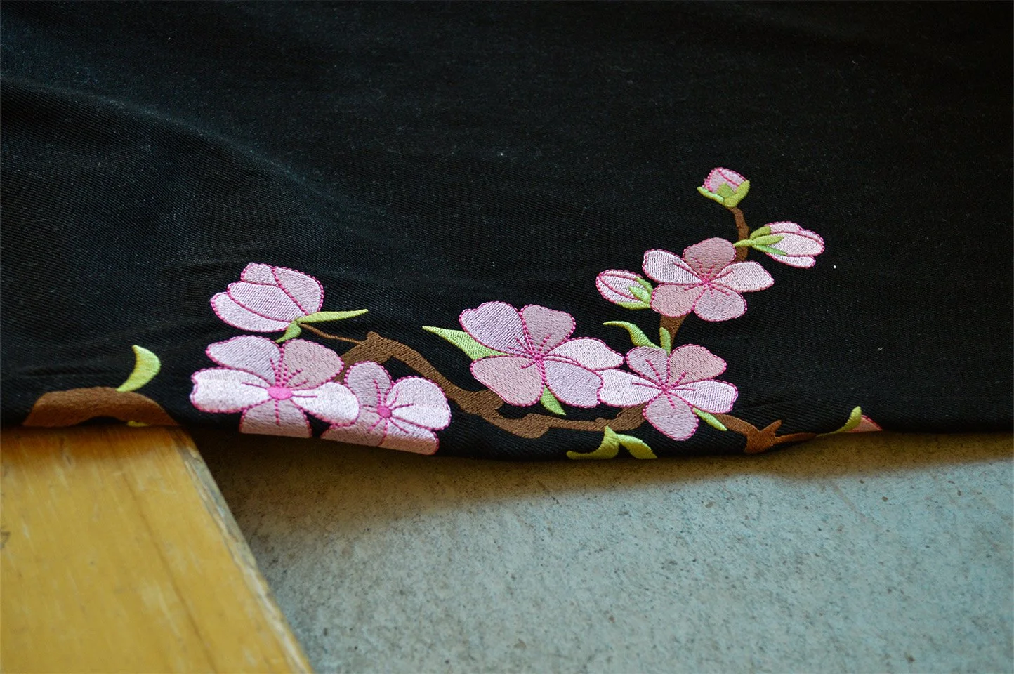 Close-up of a black fabric with embroidered pink cherry blossom flowers and green leaves.