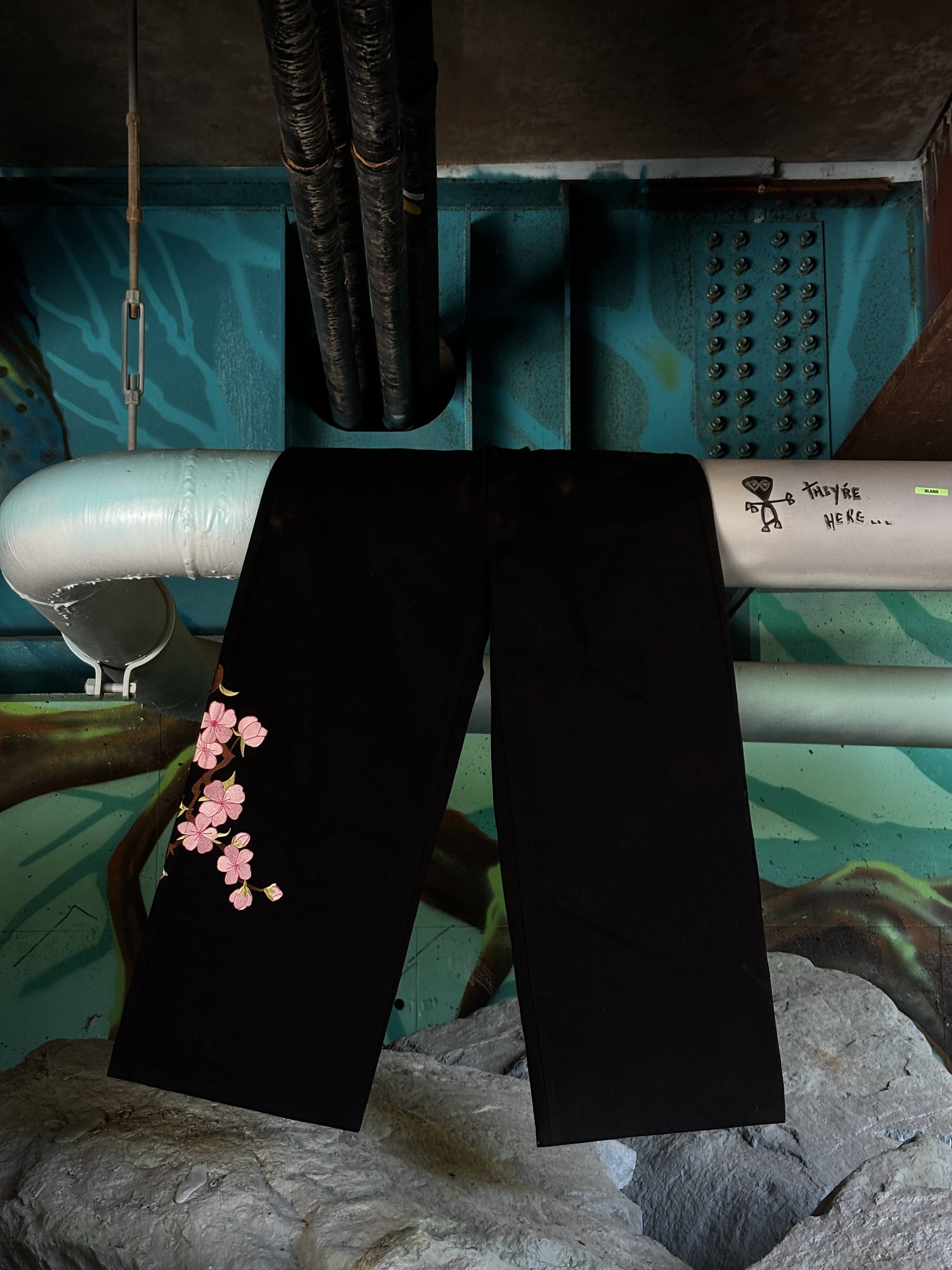 Colorful mural with rocks, pipes, and graffiti, featuring black yoga pants with pink flower design draped over a rock.