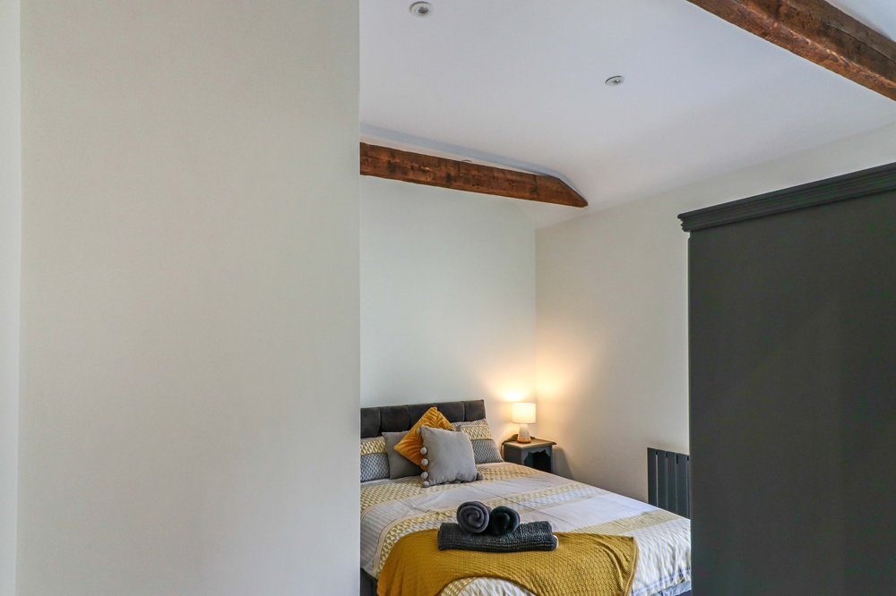 A cozy bedroom with a neatly made bed, decorative pillows, and a bedside lamp, partially visible through a doorway.