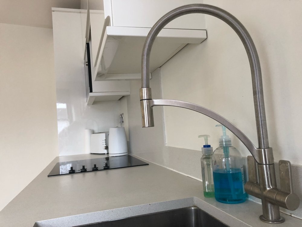 Kitchen countertop with a stainless steel faucet, soap dispenser, hand sanitizer, an electric stove, and some containers on the counter.
