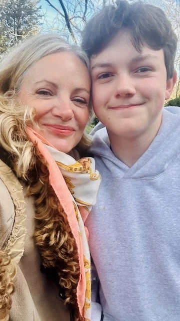 A woman and a young man smiling outdoors on a sunny day.
