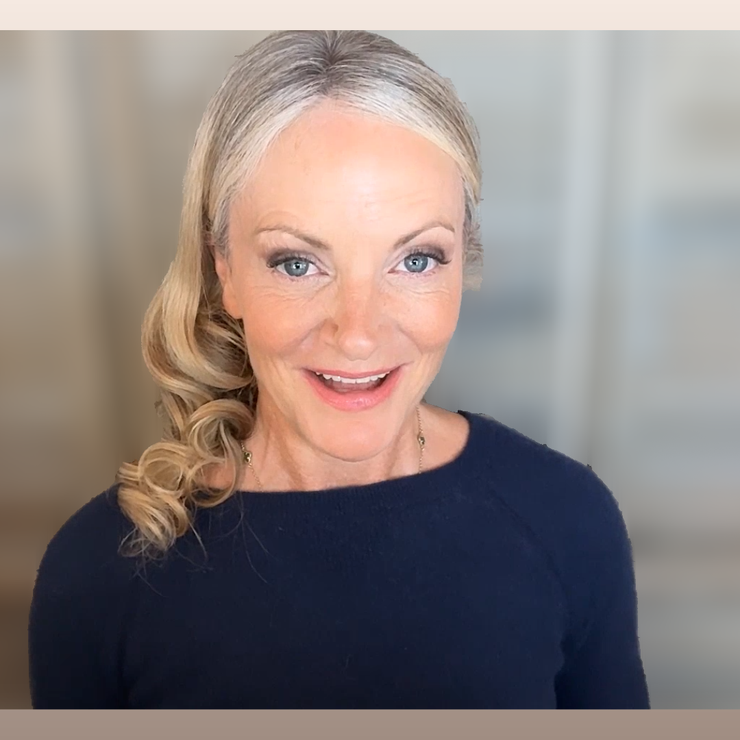 Portrait of a smiling woman with blonde, curled hair and blue eyes, wearing a navy blue top, in front of a blurred neutral background.