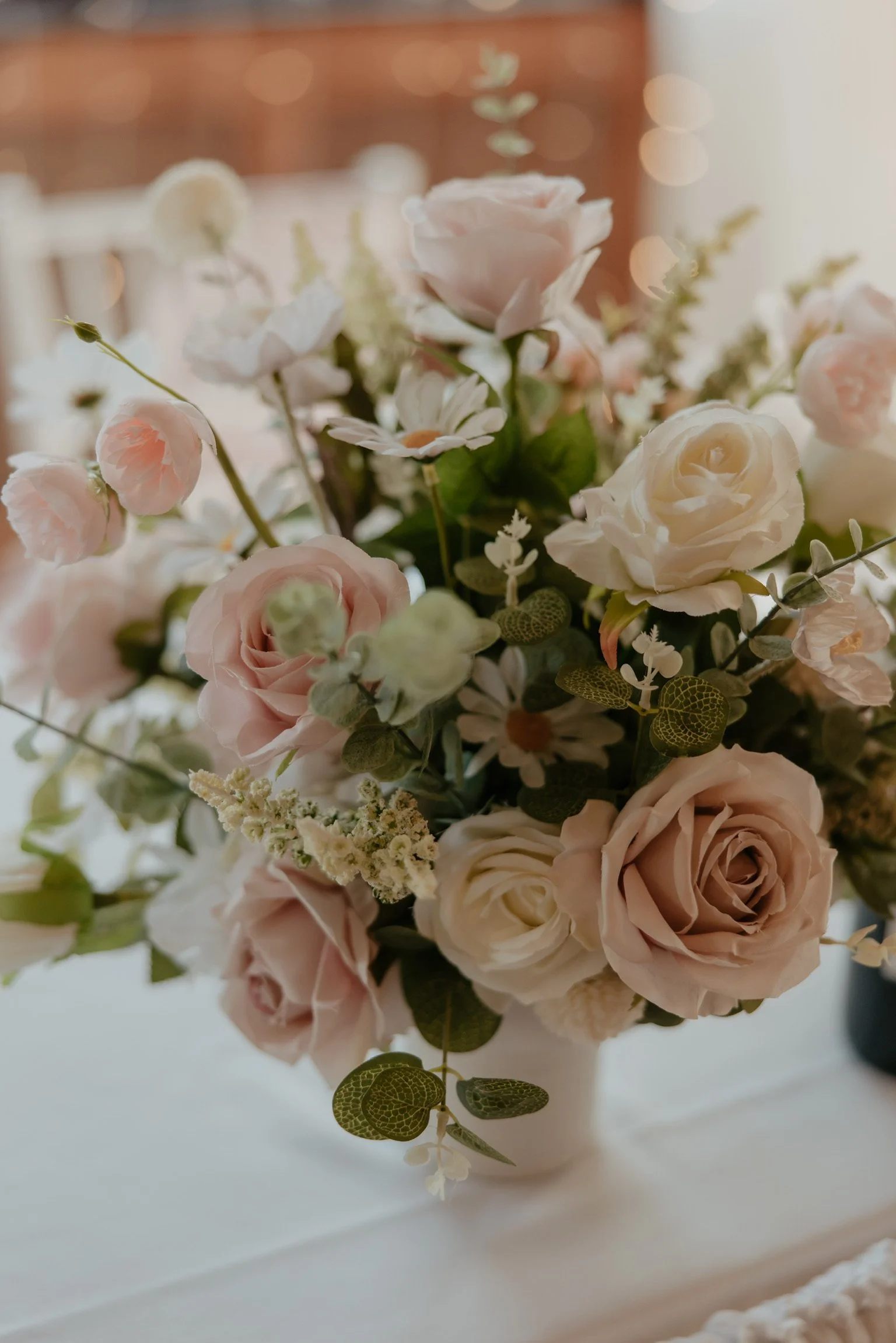 Low white bowl floral arrangement with white roses and blush pink flowers on a wedding top table.