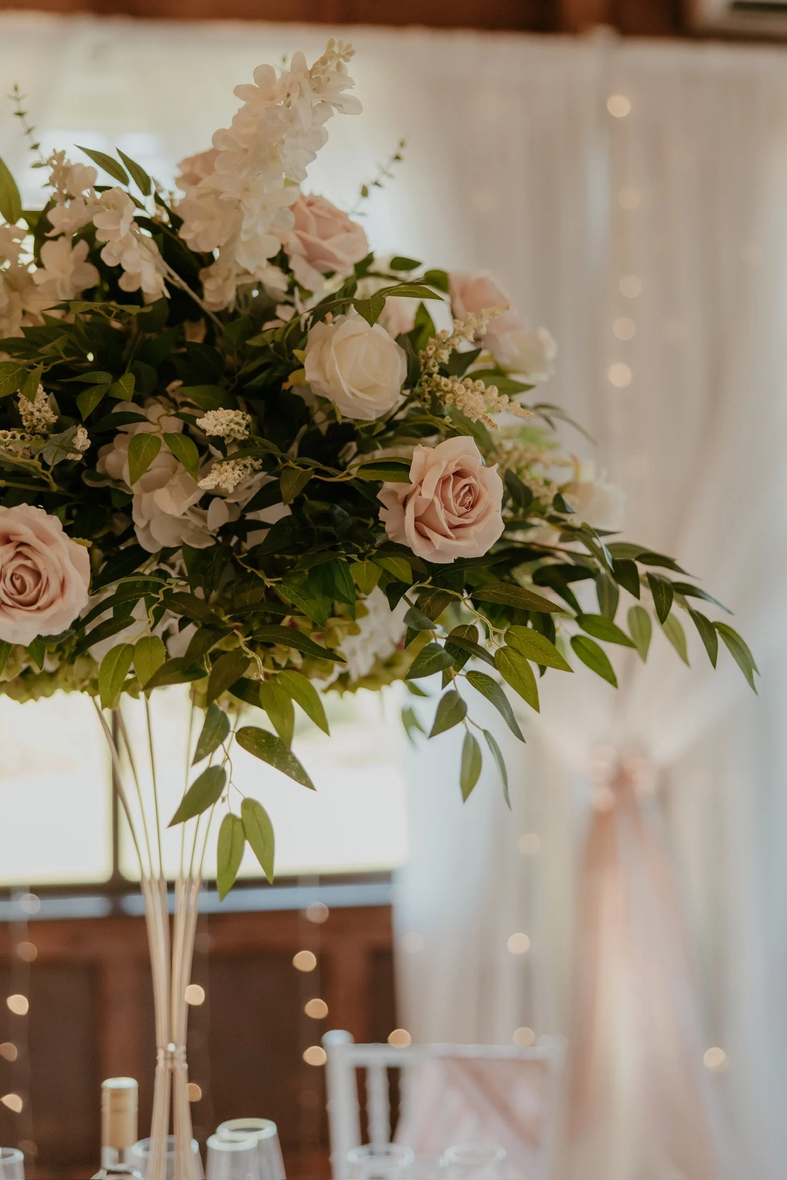 Close up of Tall gold metal centre piece vase filled with pink and white roses on a white tablecloth.