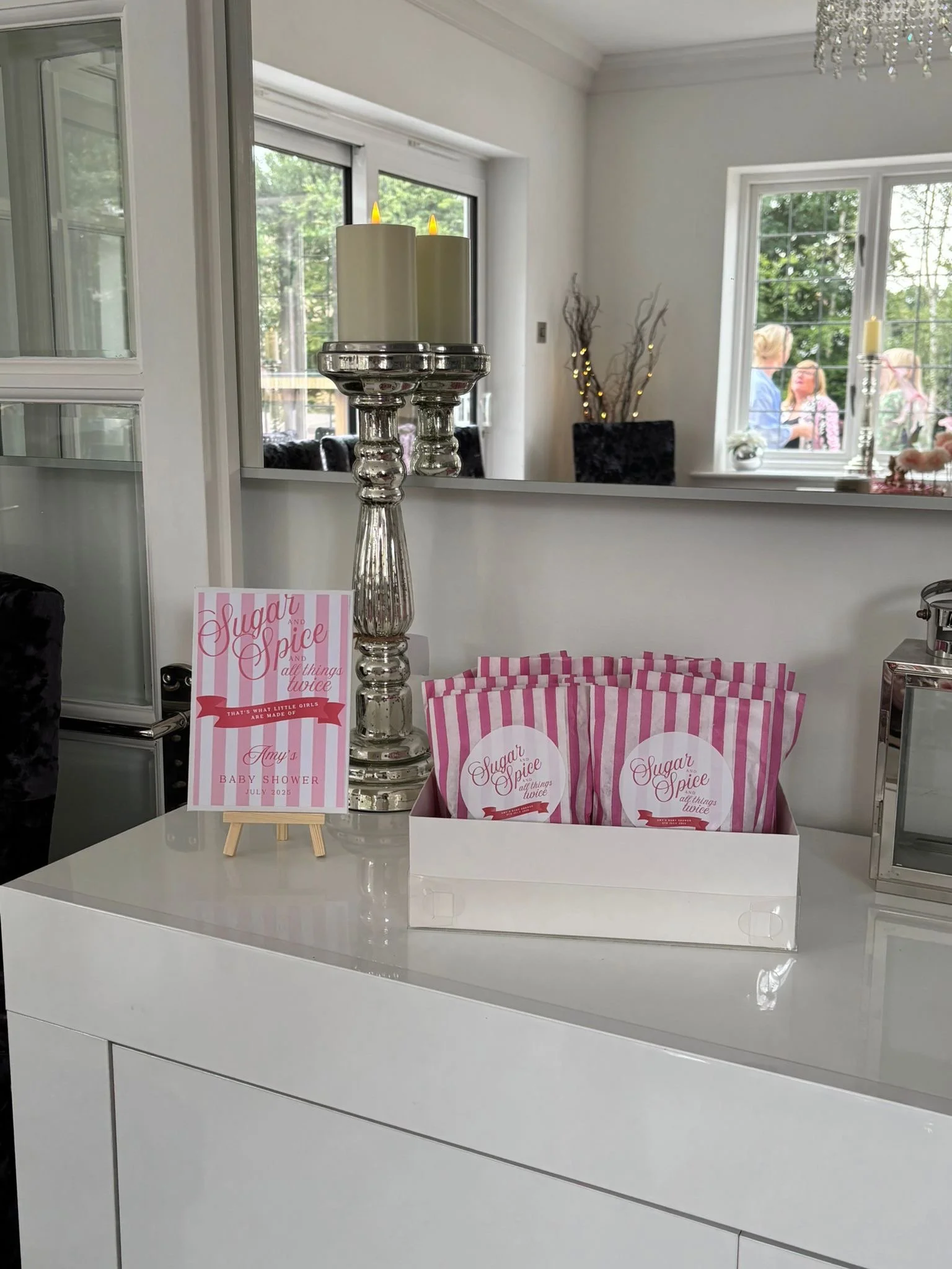 Decorative baby shower display with pink and white striped party favor bags, a silver candle holder, and a pink and white sign for a baby shower event.