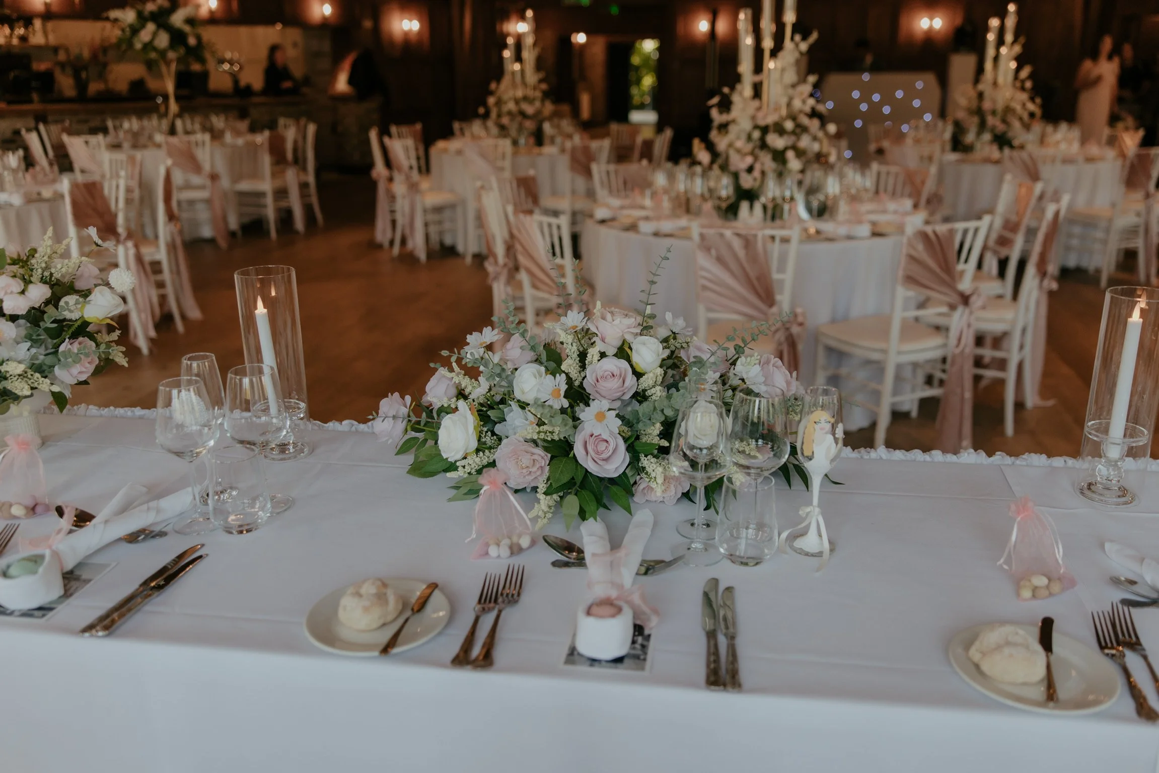 Elegant wedding reception with round tables, floral centerpieces, candles, and pastel-colored decorations in a rustic venue.