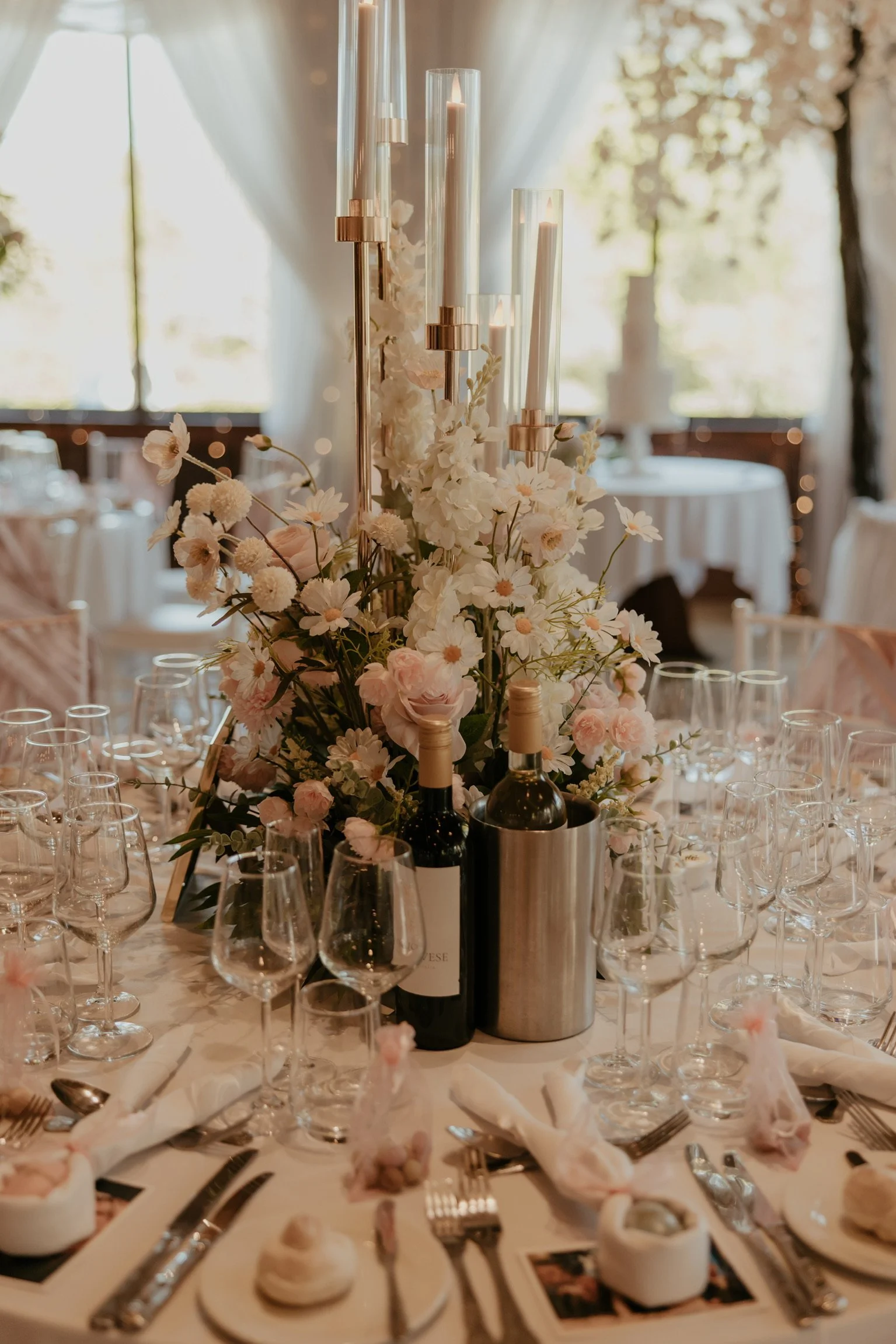 A gold candelabra centre piece surrounded by cream & pink roses, daisies, and Led candles. 