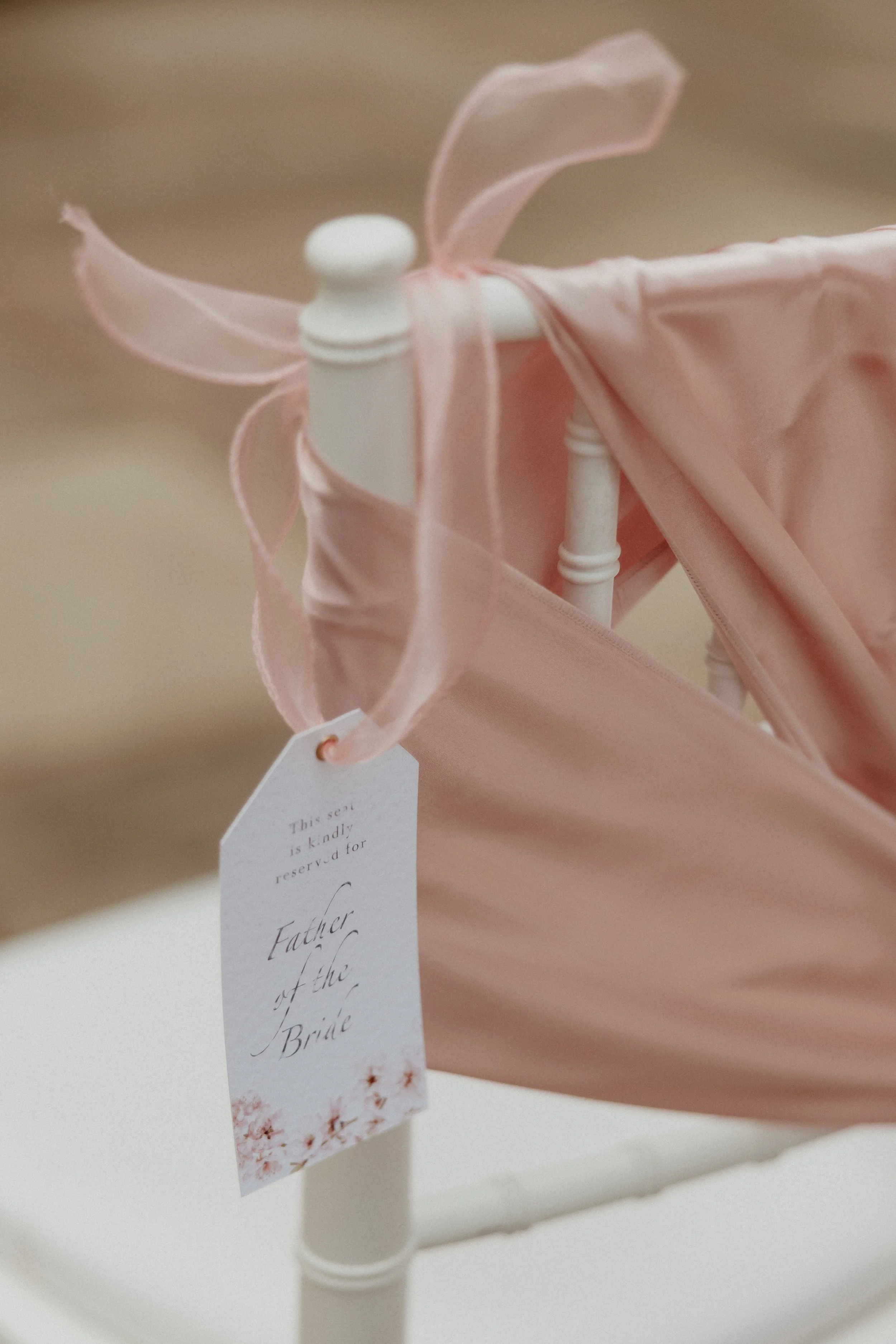 A white chair with a pink fabric draped over it, tied with a pink ribbon. A reserved sign for the Father of the Bride is attached to the chair.