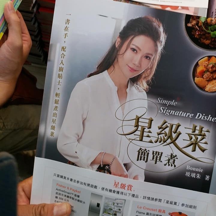 A woman in a white shirt smiling on the cover of a cookbook with Chinese and English text, featuring pictures of prepared dishes.