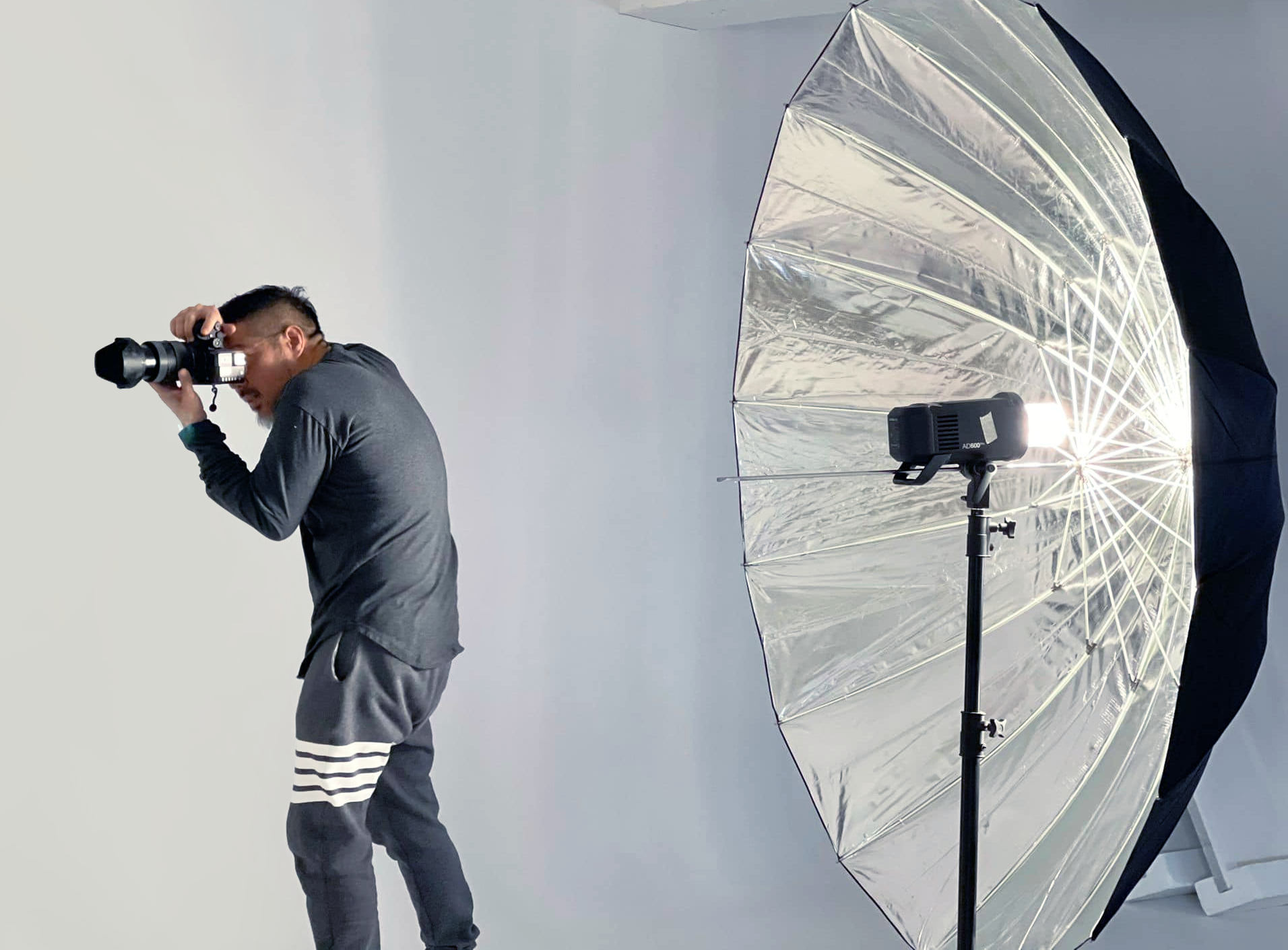 Photographer taking a photo in a studio with a large silver reflective umbrella light.