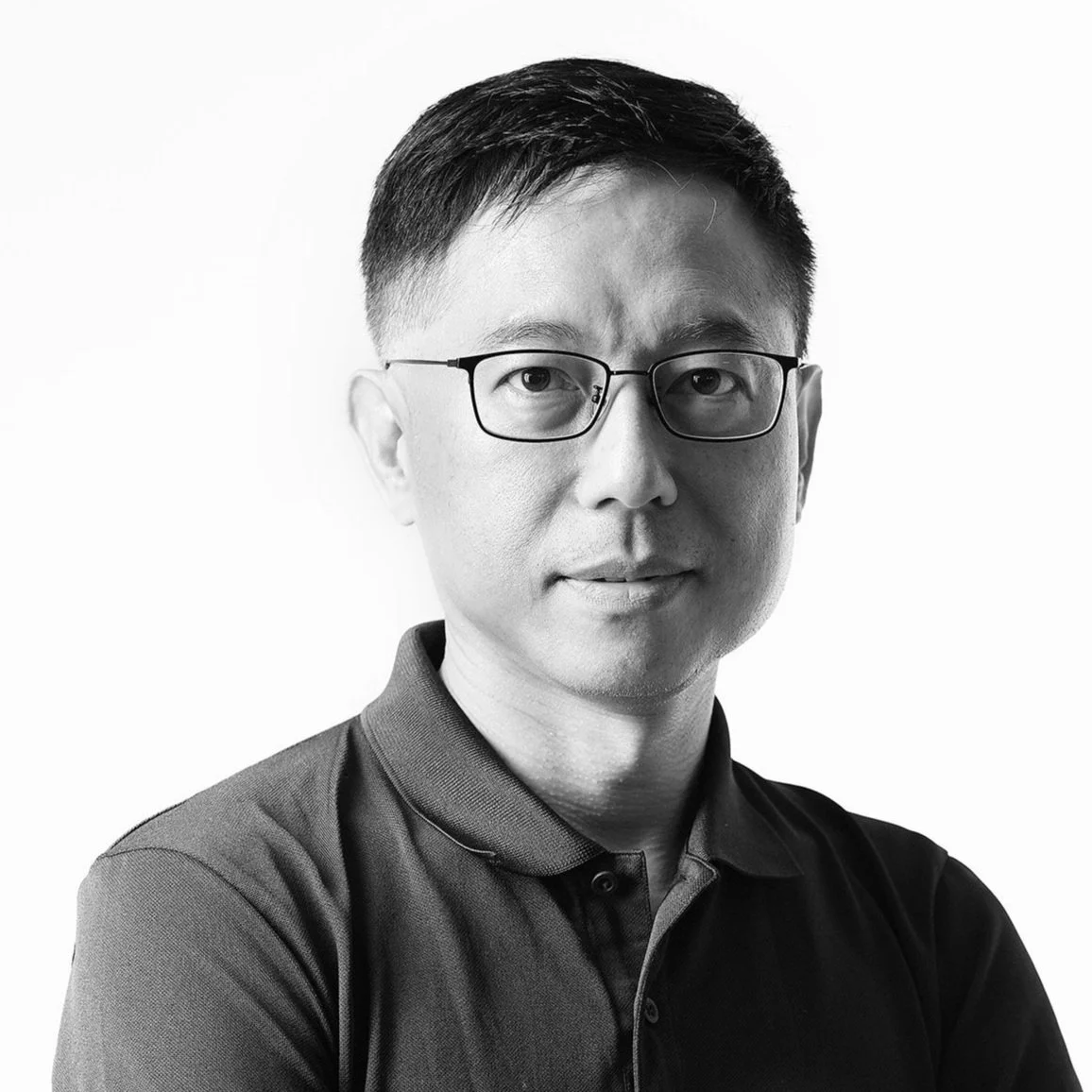 Black and white portrait of an Asian man with short hair and glasses, wearing a collared shirt, against a plain background.